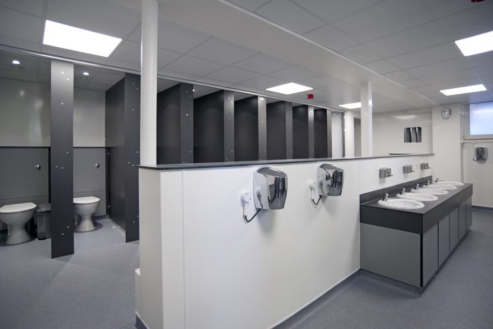 grey unisex washroom with full height privacy cubicles with half height ducting, a communal hand wash vanity and hand dryers at princes risborough school.jpg