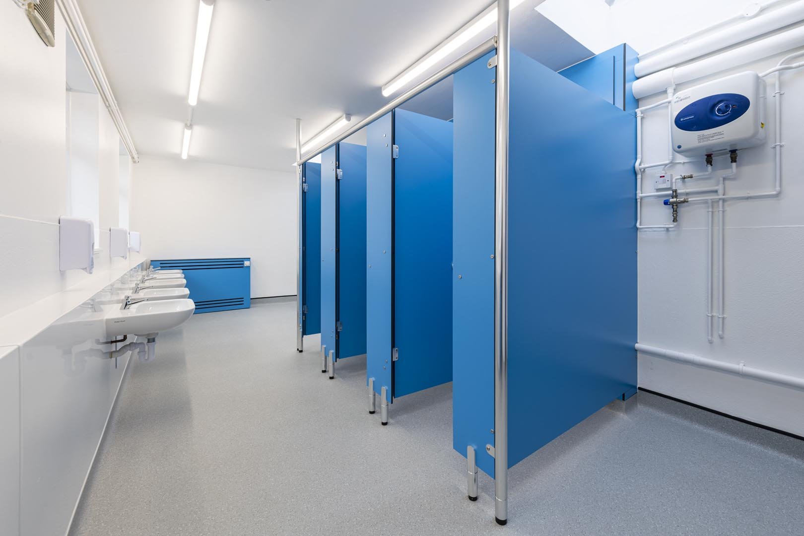 a washroom with blue cubicles and a row of wall mounted sinks and walls with hygienic wall cladding at howard junior school.jpg