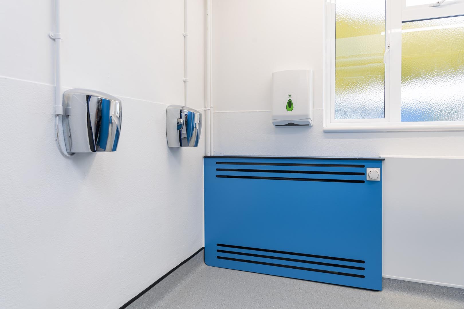 blue radiator cover and chrome hand dryers on white hygeinic wall cladding at howard junior school.jpg