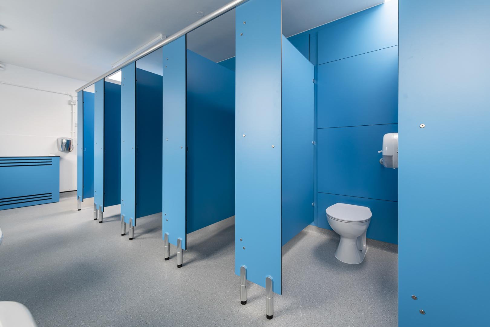 row of blue toilet cubicles and full height duct panels and a radiator cover at howard junior school.jpg