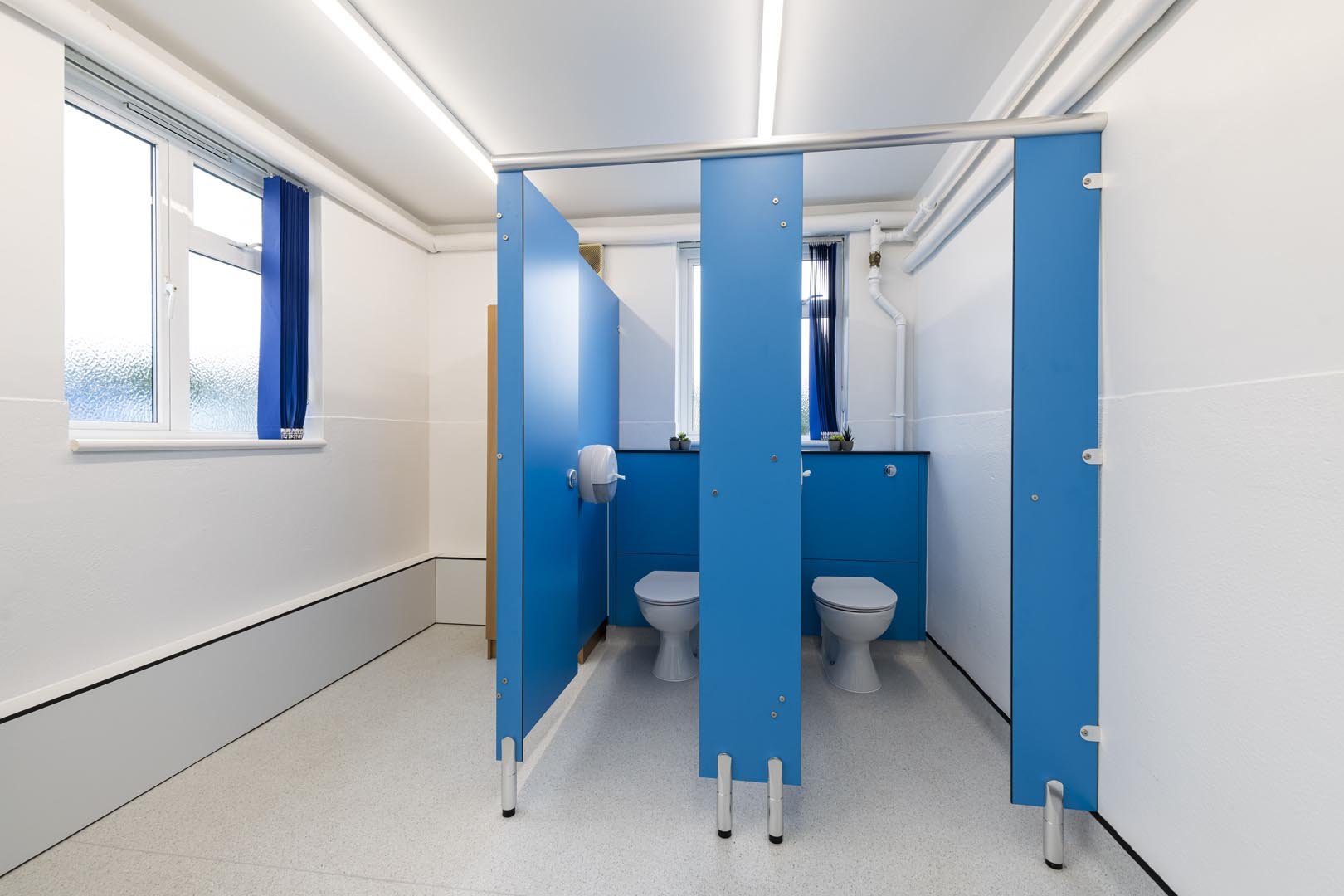 two toilet cubicles in blue colour with half height ducting in washrooms at howard junior school.jpg
