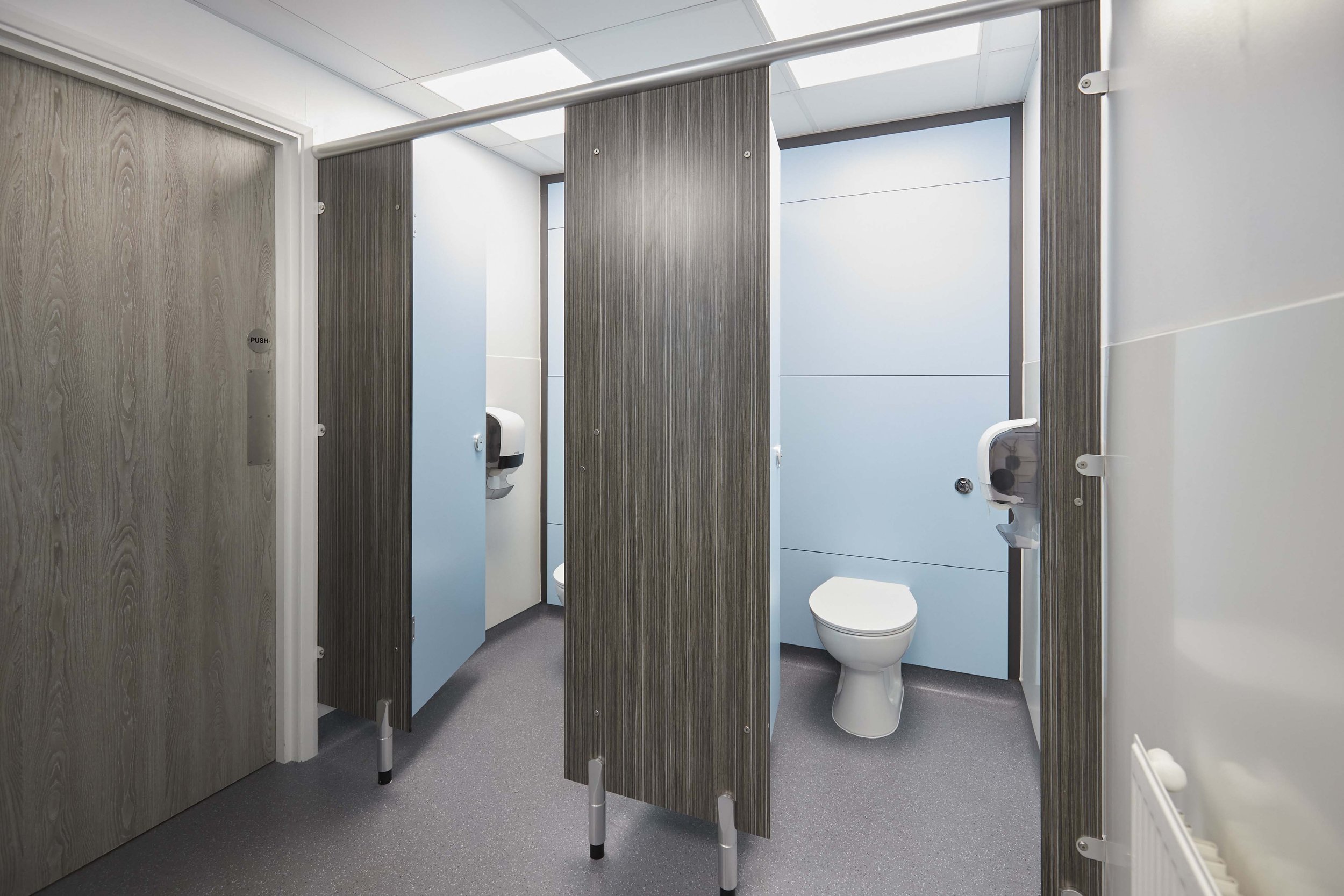 two toilet cubicles with blue duct panels and doors and woodgrain pilasters at box hill school.jpg