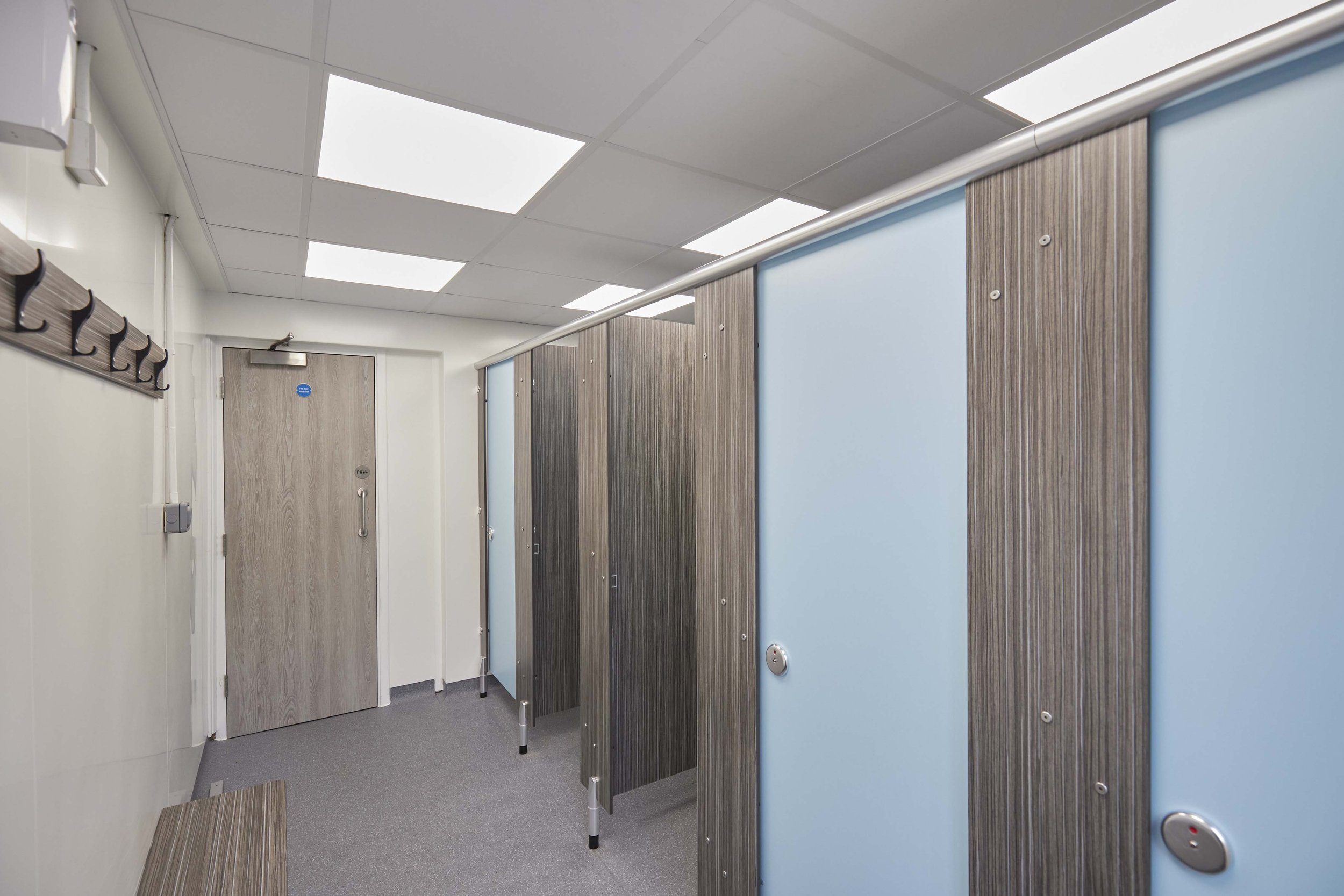 row of shower cubicles in blue and woograin colour with benching and pegs opposite at box hill school.jpg