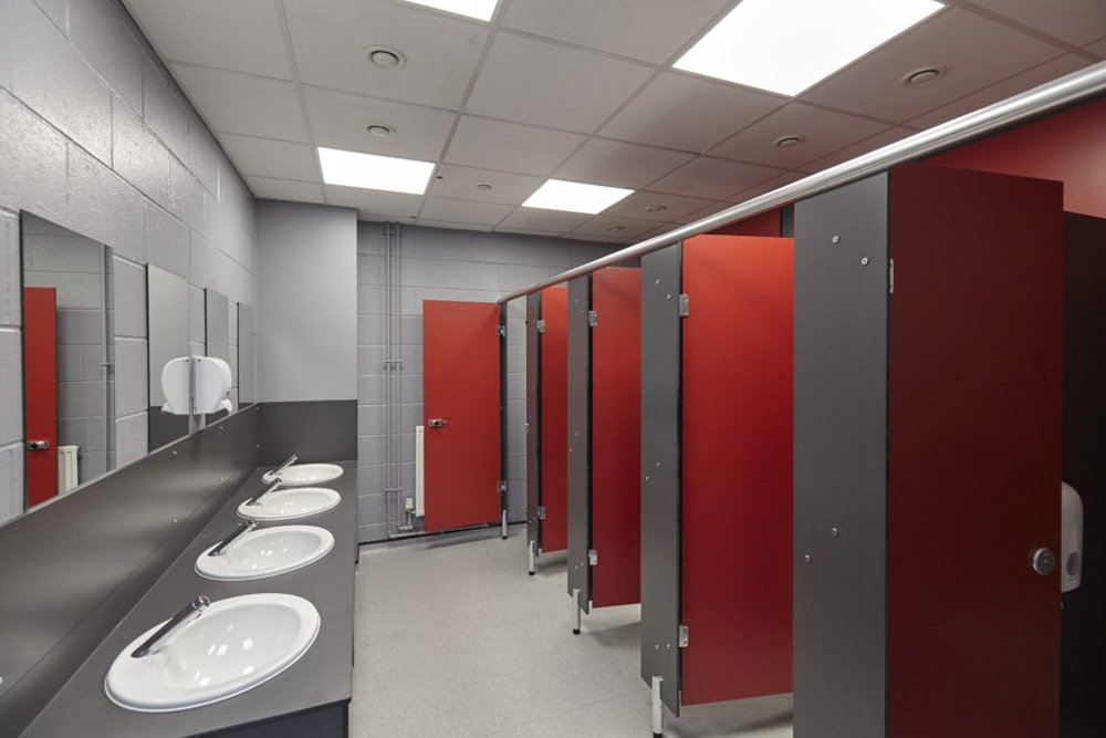 grey and red toilet block at ark acton with toilet cubicles, a vanity unit and mirrors.jpg