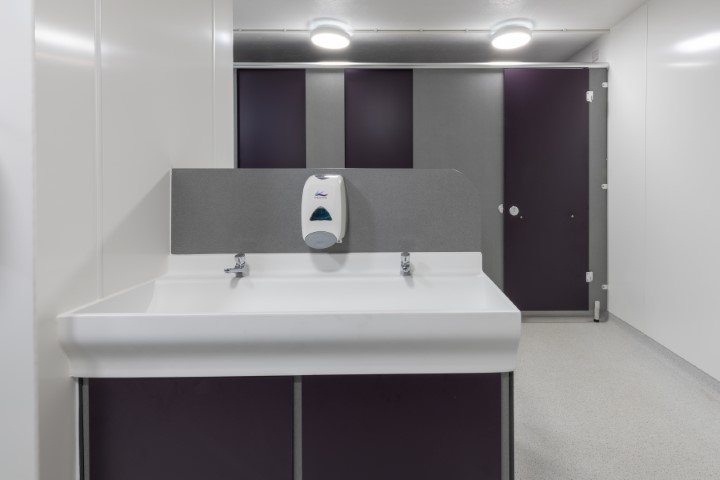 hand wash area with vanity unit and trough with toilets behind at fakenham academy.jpg