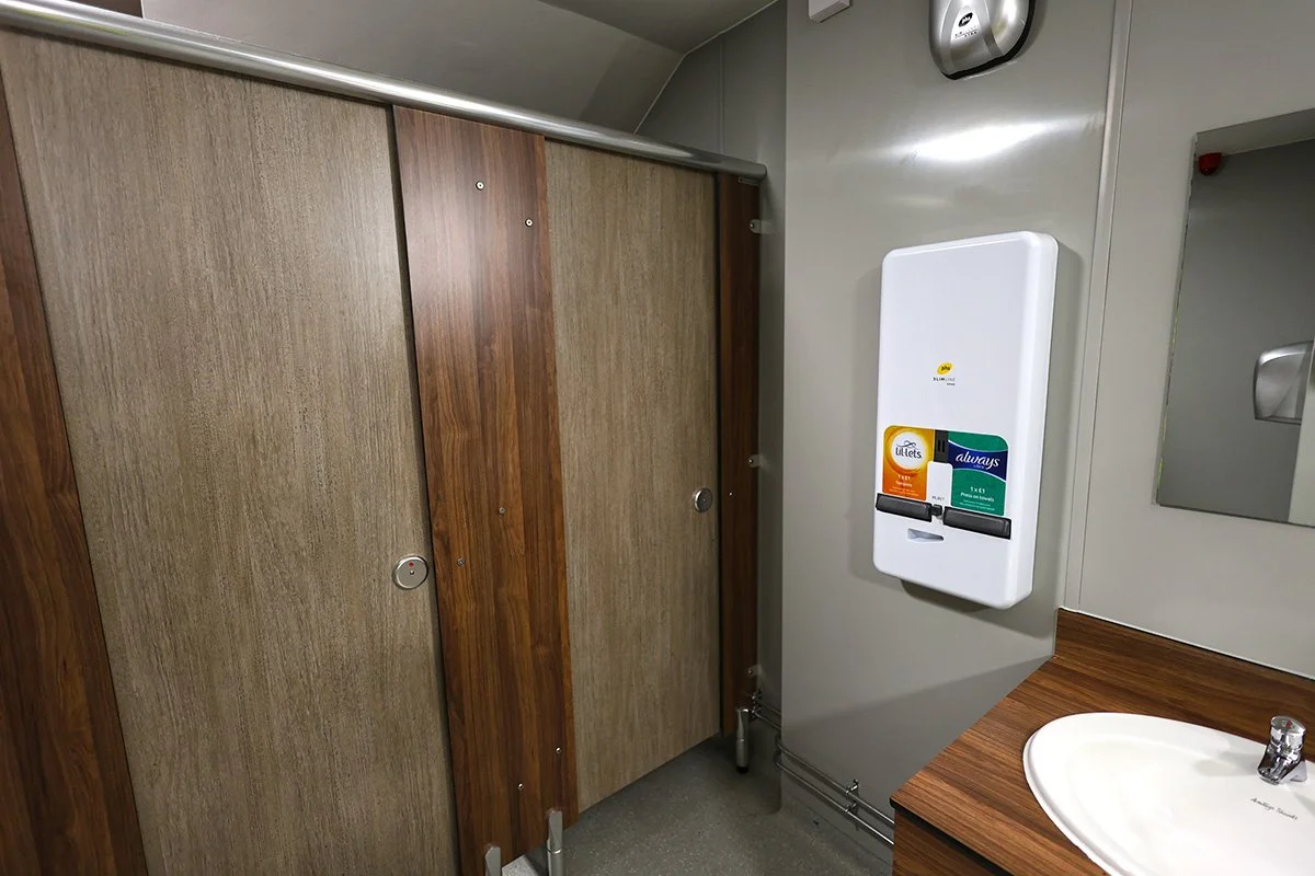 Womans sanitary dispenser alongside wooden style cubicles at holiday park.jpg