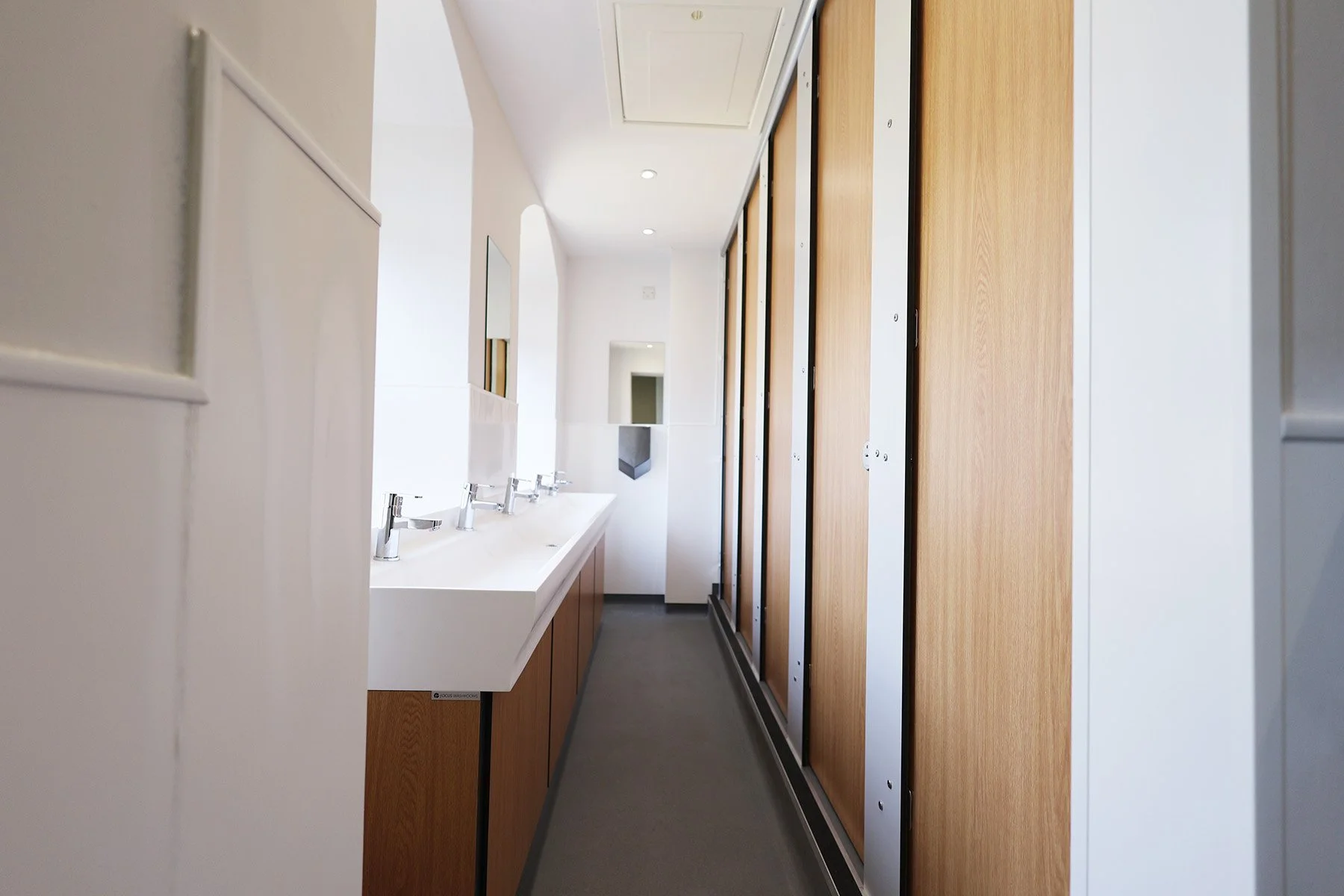 Corridor with closed cubicle doors and trough basin at Lancing College.jpg