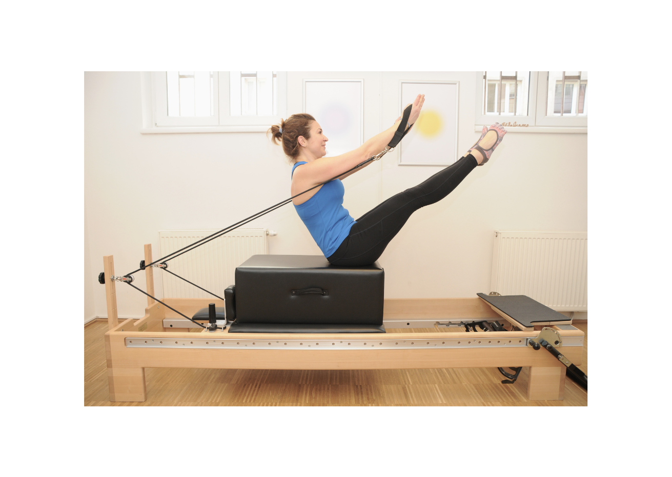 Frau auf Pilates-Reformer in Yoga-Position mit Kabelzug.