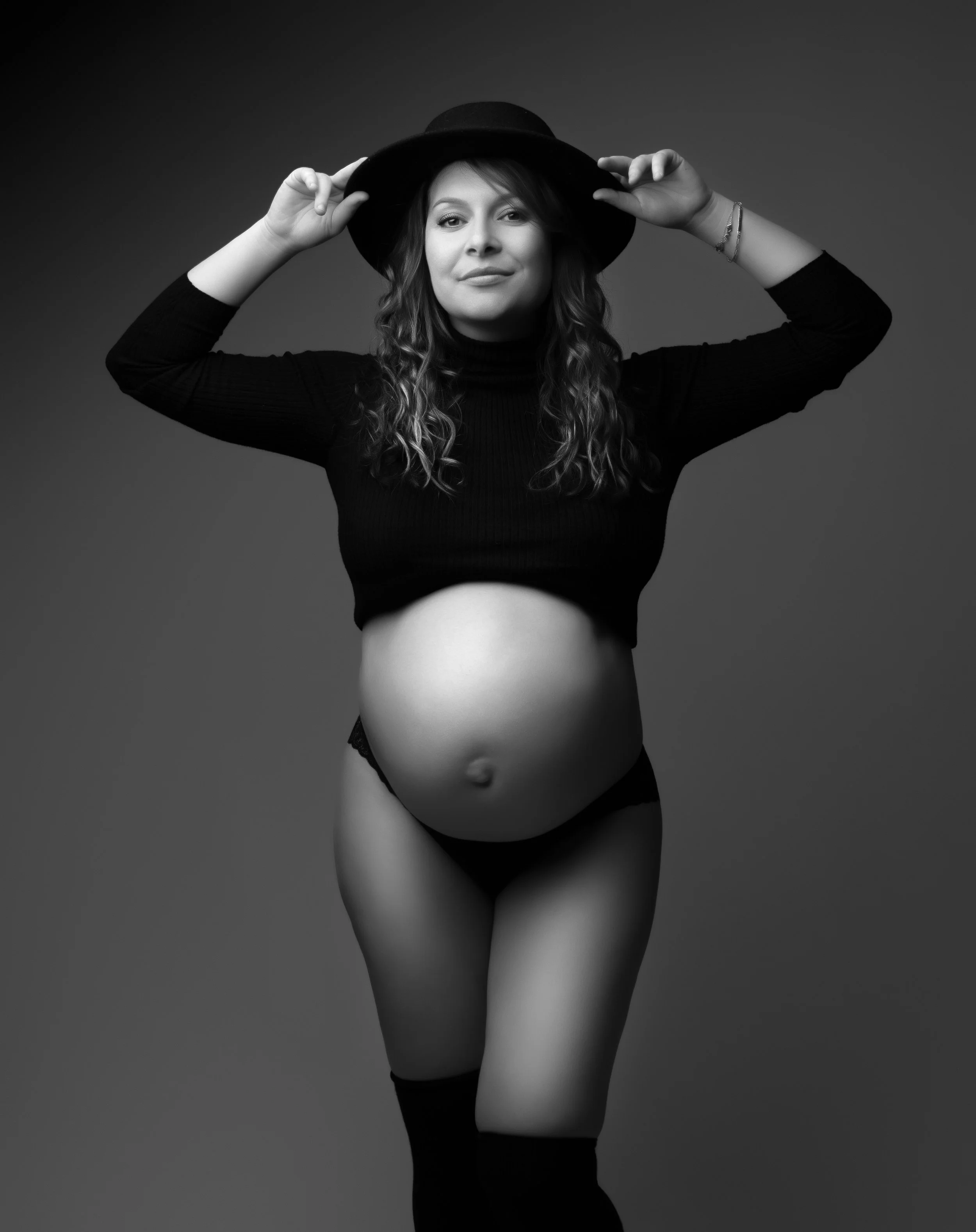 Femme enceinte portant un chapeau, debout, en sous-vêtements noirs, en noir et blanc.