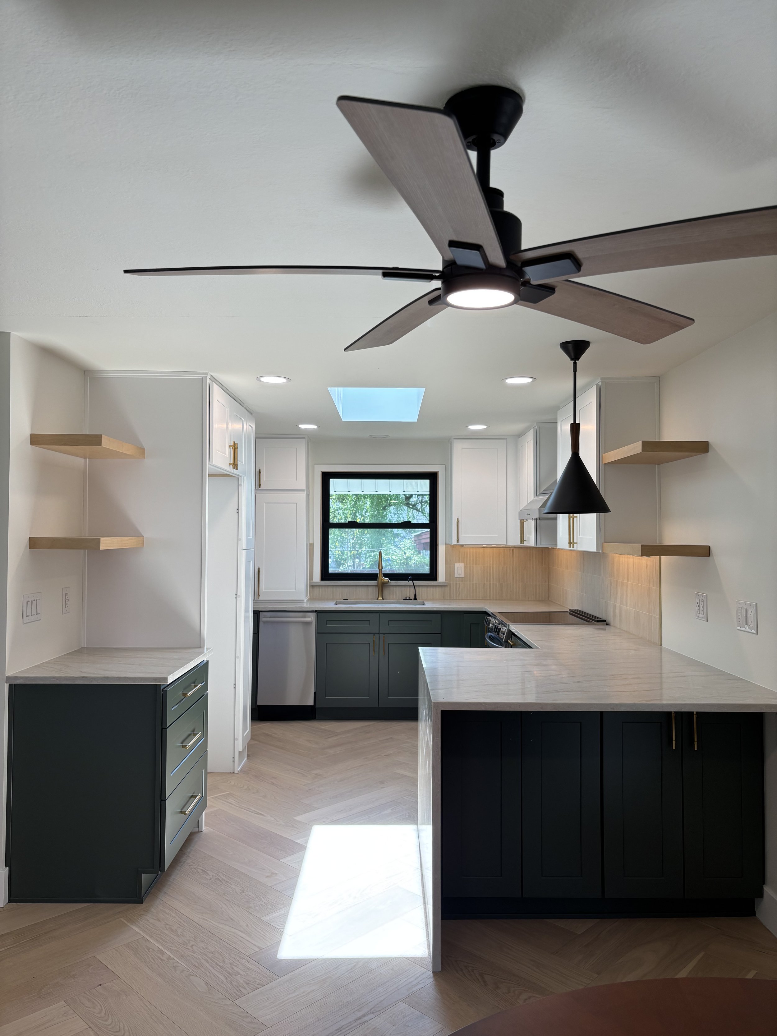 Modern kitchen with dark green and white cabinets, light wood countertops, and a ceiling fan.