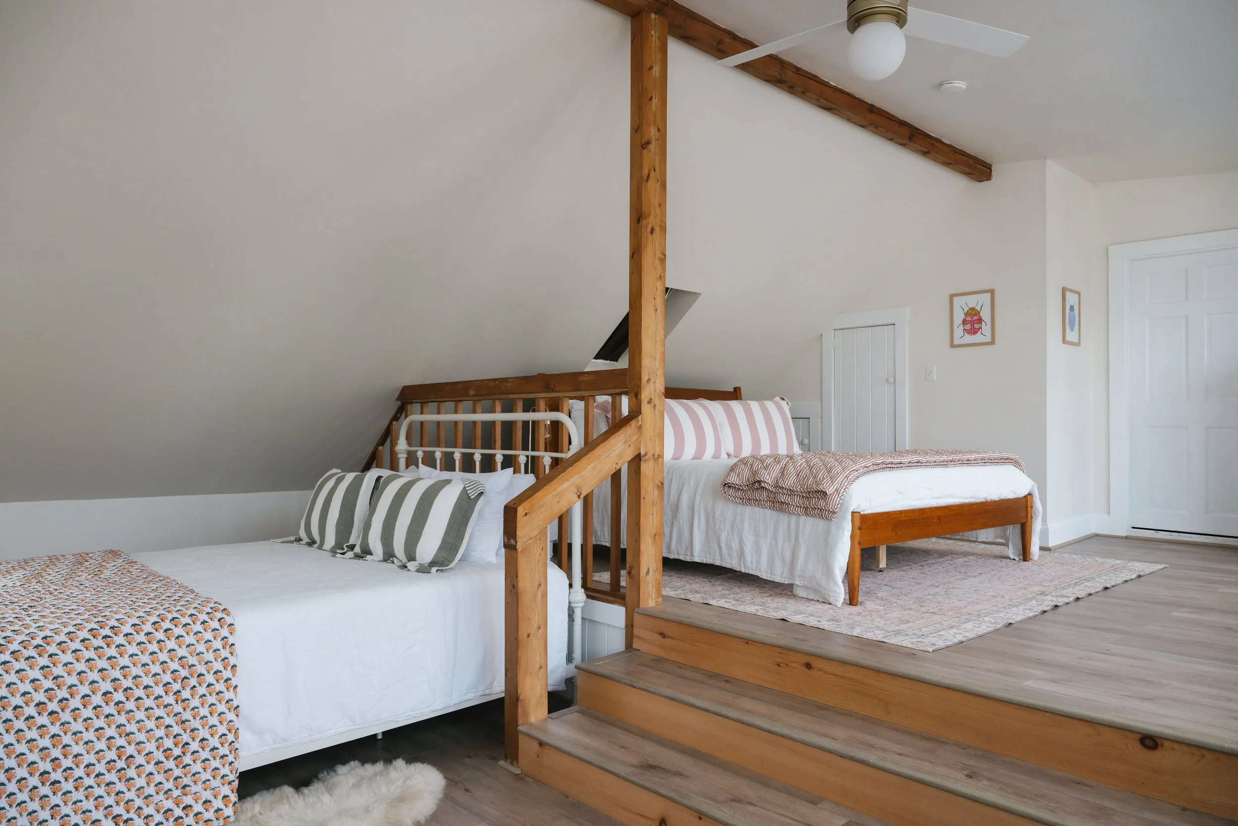 Two beds in an attic bedroom with sloped ceiling, wood beams, and minimal decor.