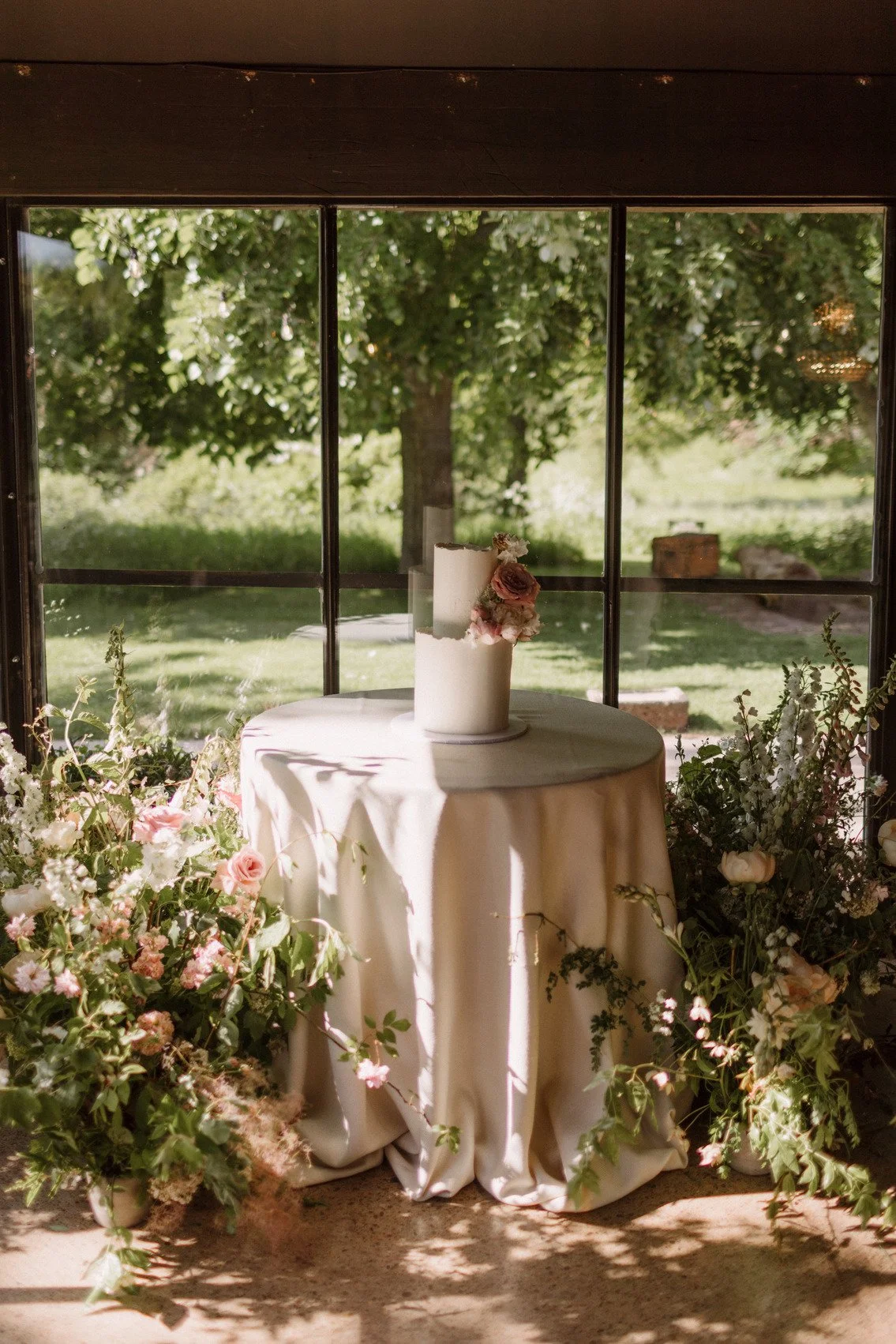 Elegant wedding cake on a round table with floral decorations and a scenic outdoor view.