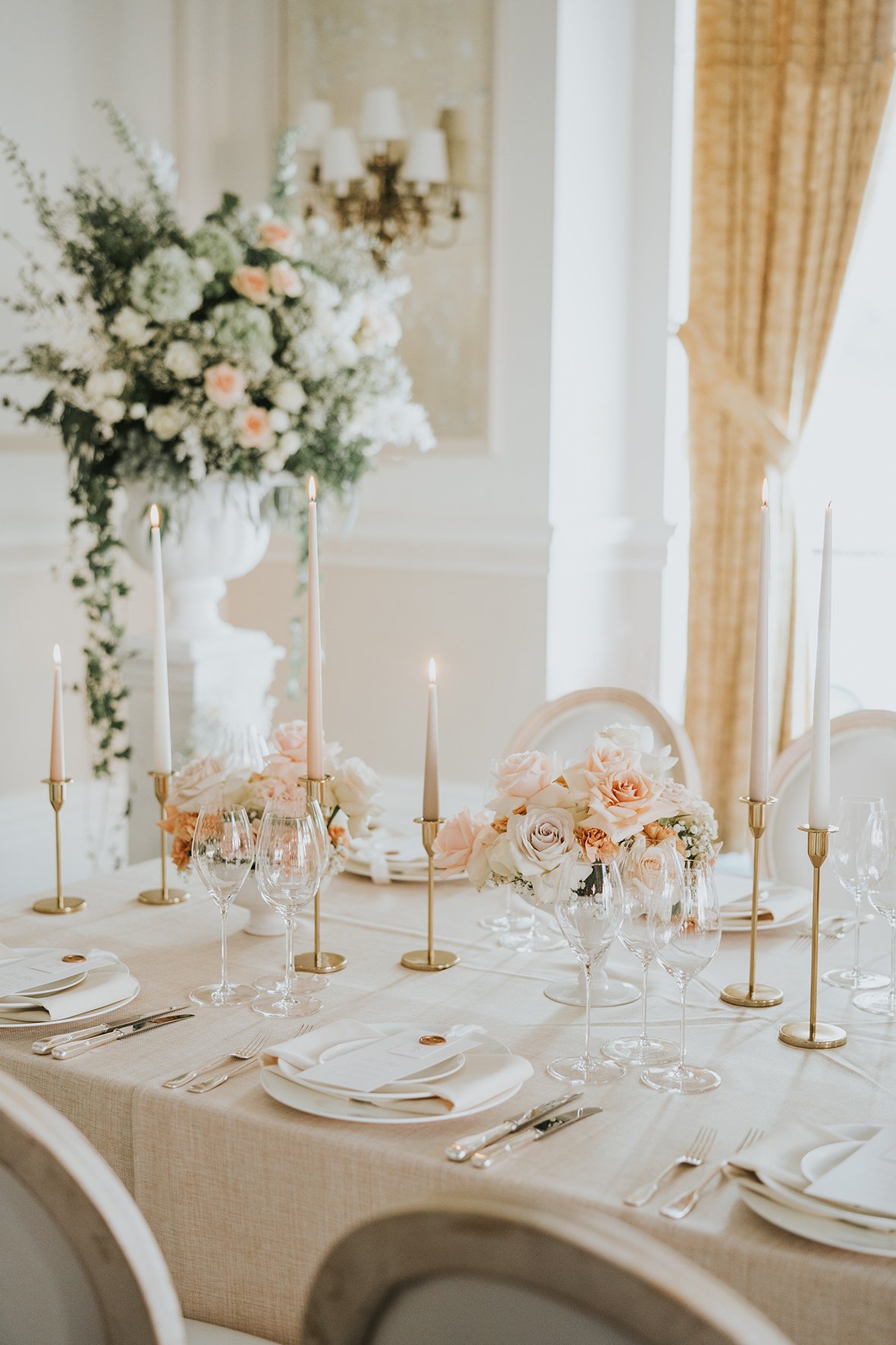 Elegant table setting with white and blush flowers, gold candlesticks, and fine glassware.