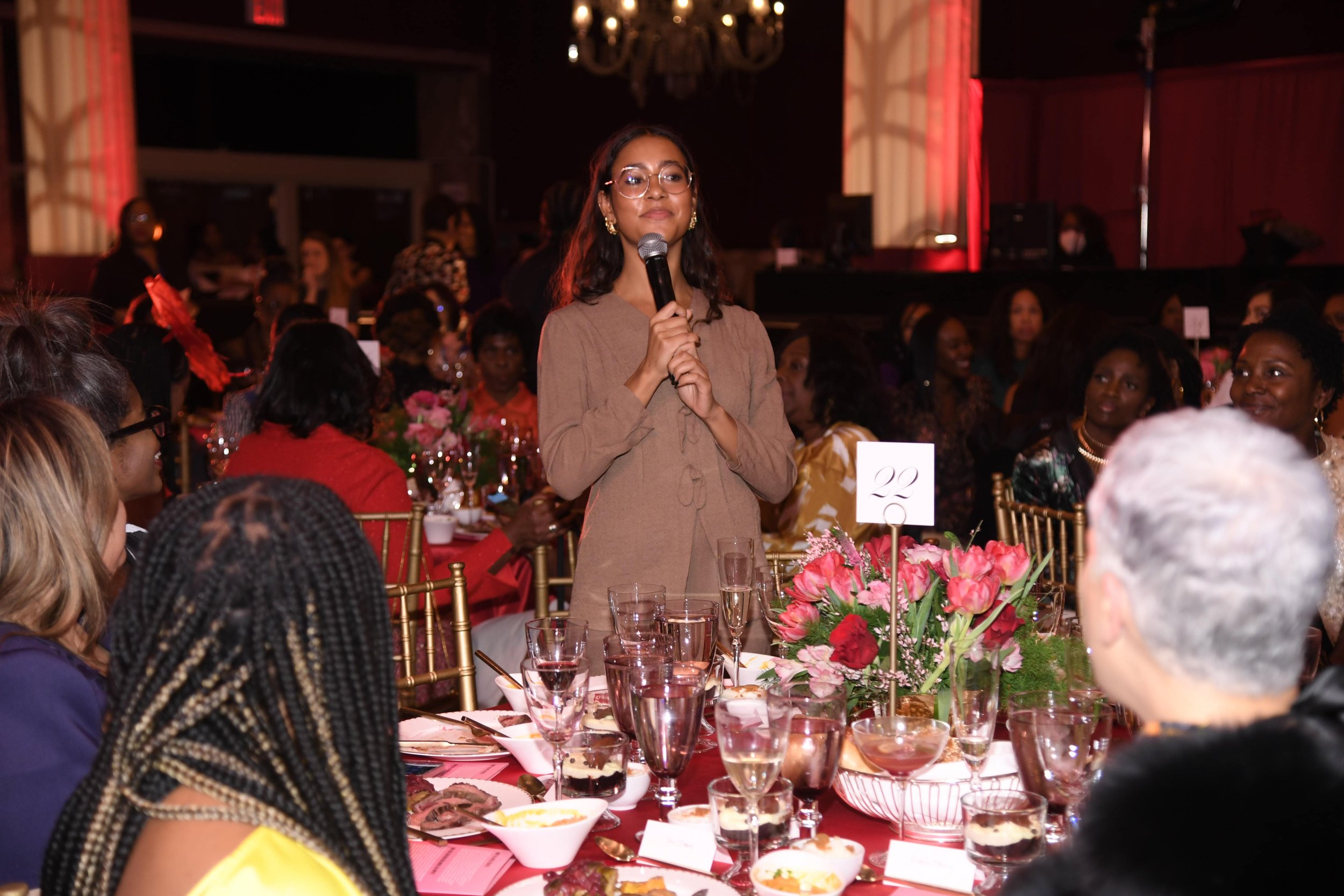 A Black woman standing at a table talking with a microphone