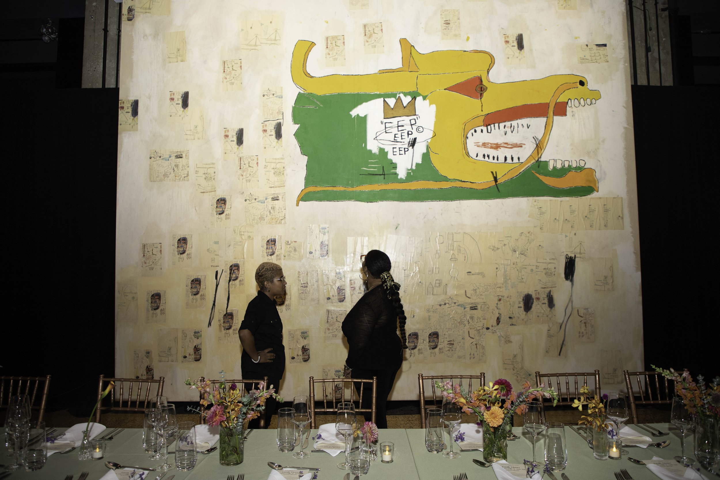 Two people standing in front of a wall with Basquiat art