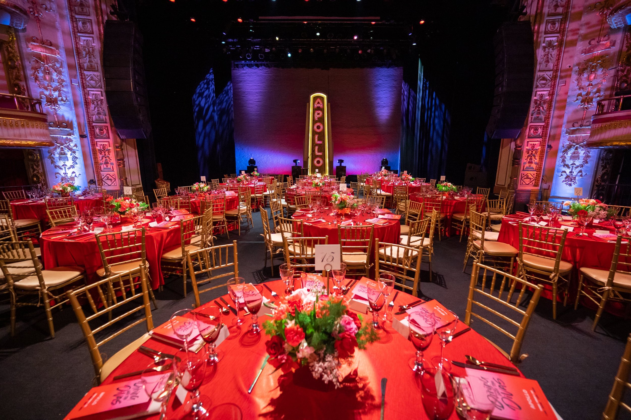 A larage theater with tables with red table cloths and red and pink floral arrangements