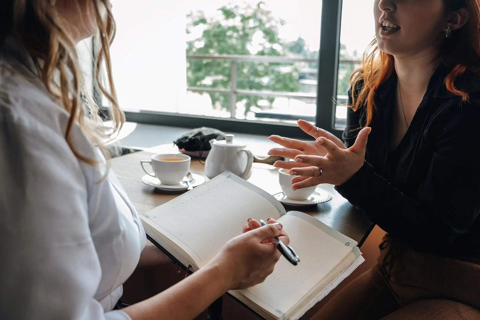 Two women sit at a table, speaking openly while the other listens and takes notes. Learn how IFS therapy in St. Louis, MO can help. An IFS therapist in St. Louis, MO, who also speaks Enneagram can track your patterns.