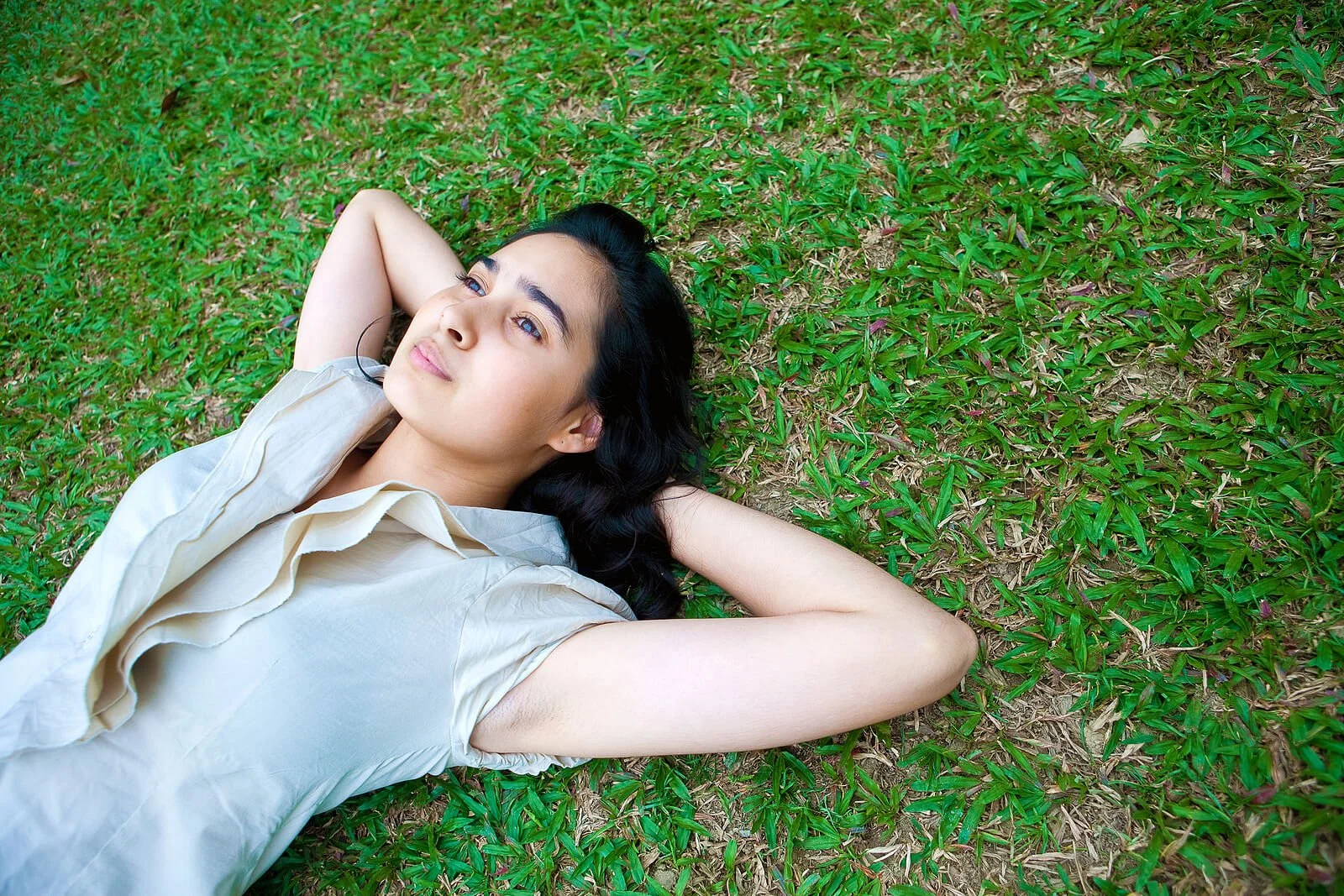 A young woman lies on the grass with her hands behind her head, gazing upward in quiet, open reflection. Learn how IFS therapy in St. Louis, MO can offer support. Explore internal family systems therapy in St. Louis, MO.