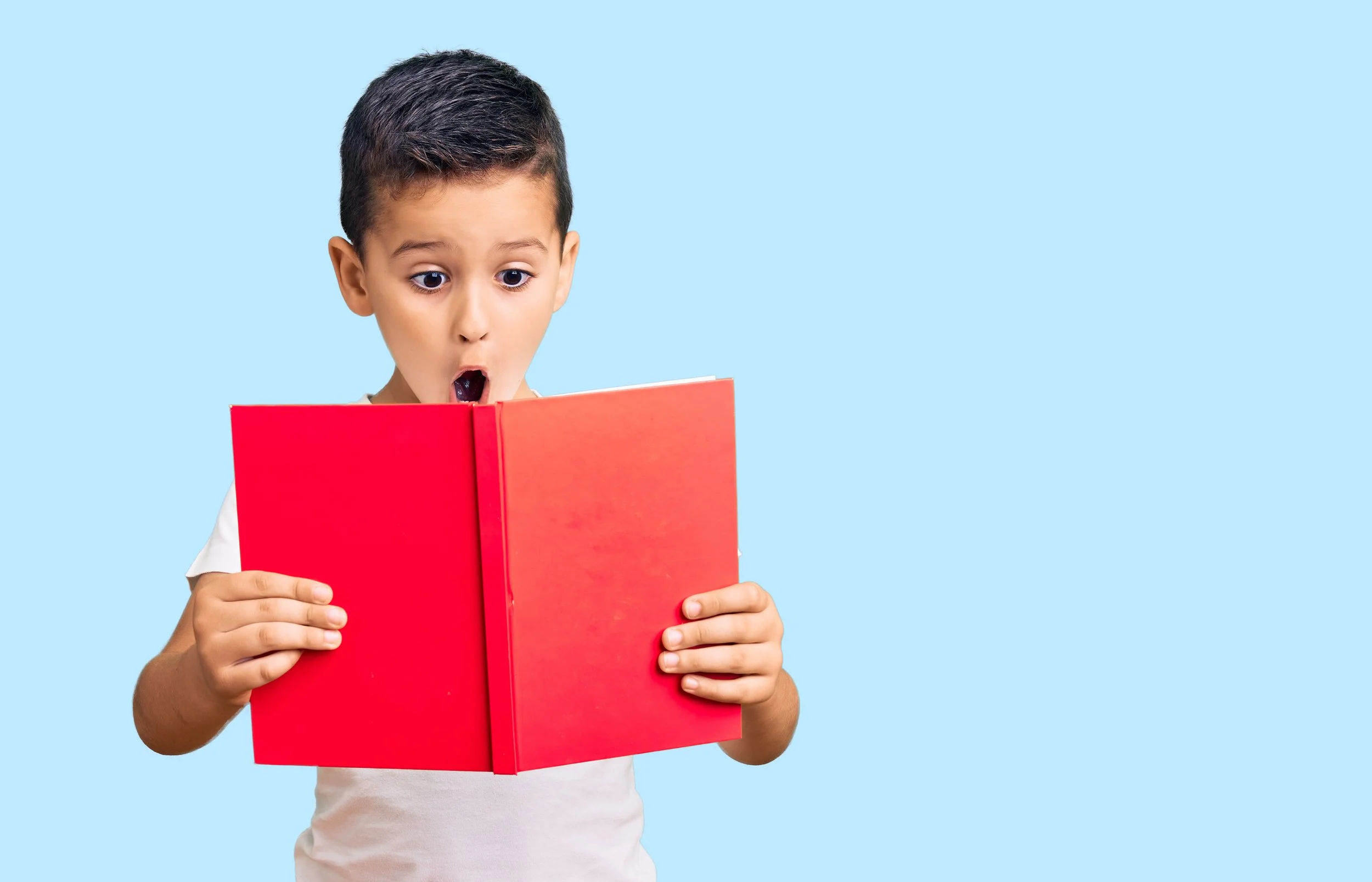 Young boy with surprised expression reading a large red book against a light blue background.