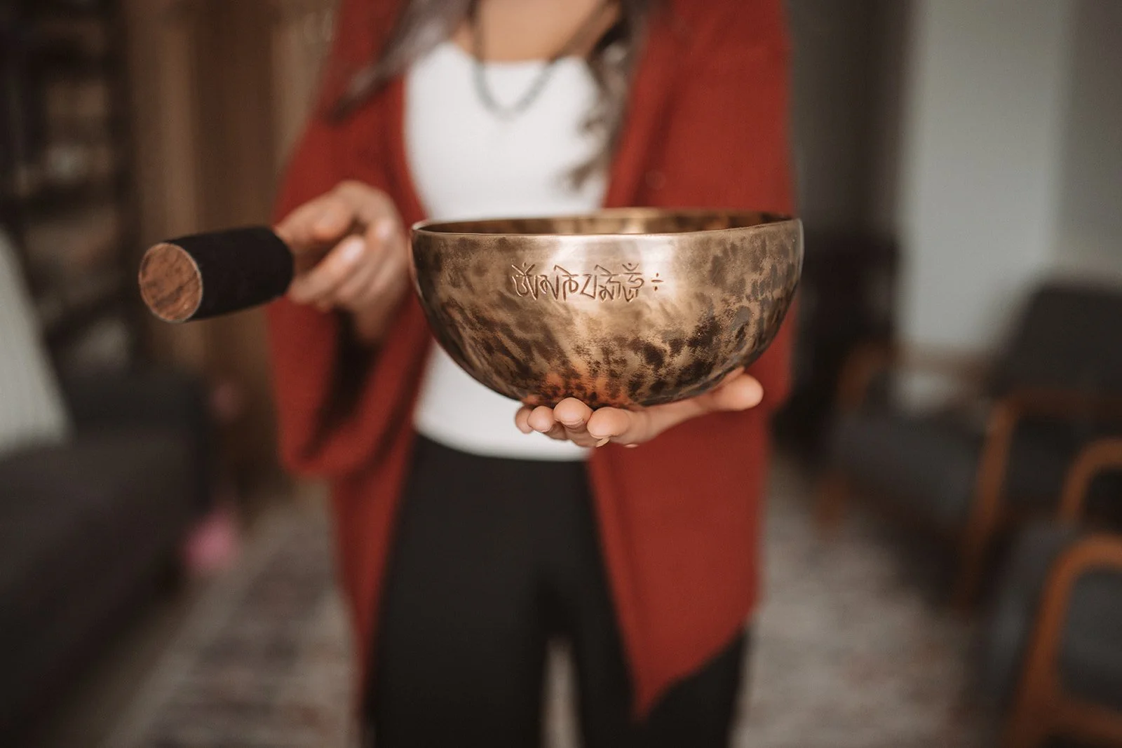 Person holding a Tibetan singing bowl inscribed with Tibetan script, with a mallet in the background.