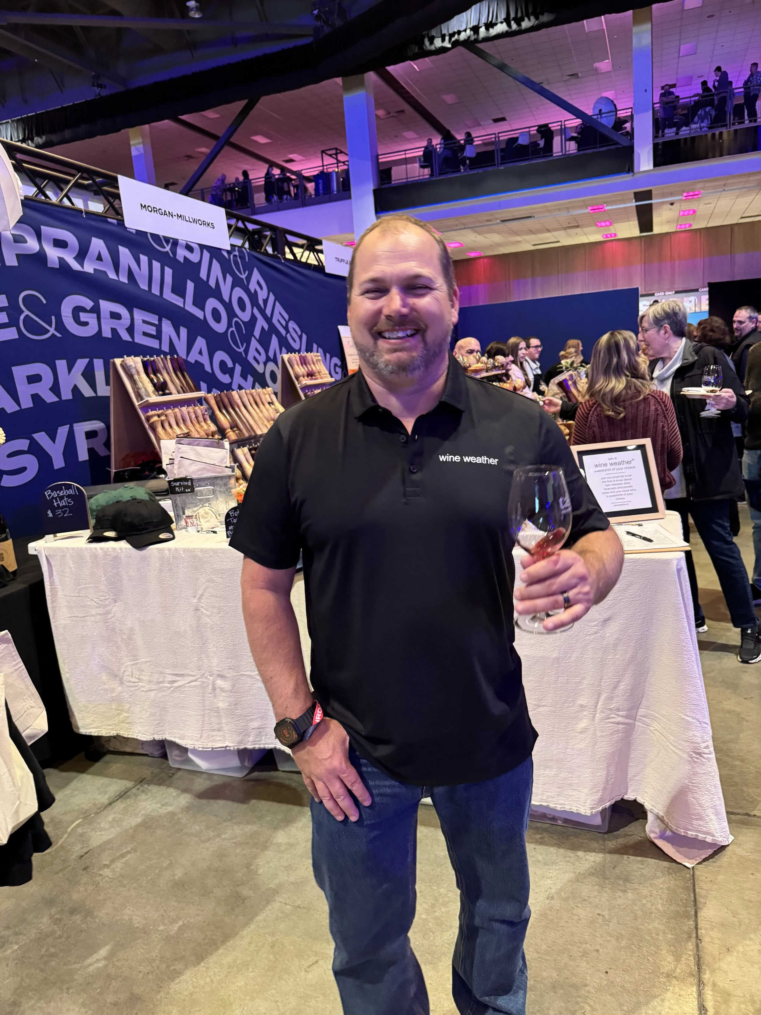 a man in wine weather's new men's polo shirt with wine weather embroidered on the left chest. Enjoying a glass of wine at the taste washington event at Lumen field celebrating washington wine month