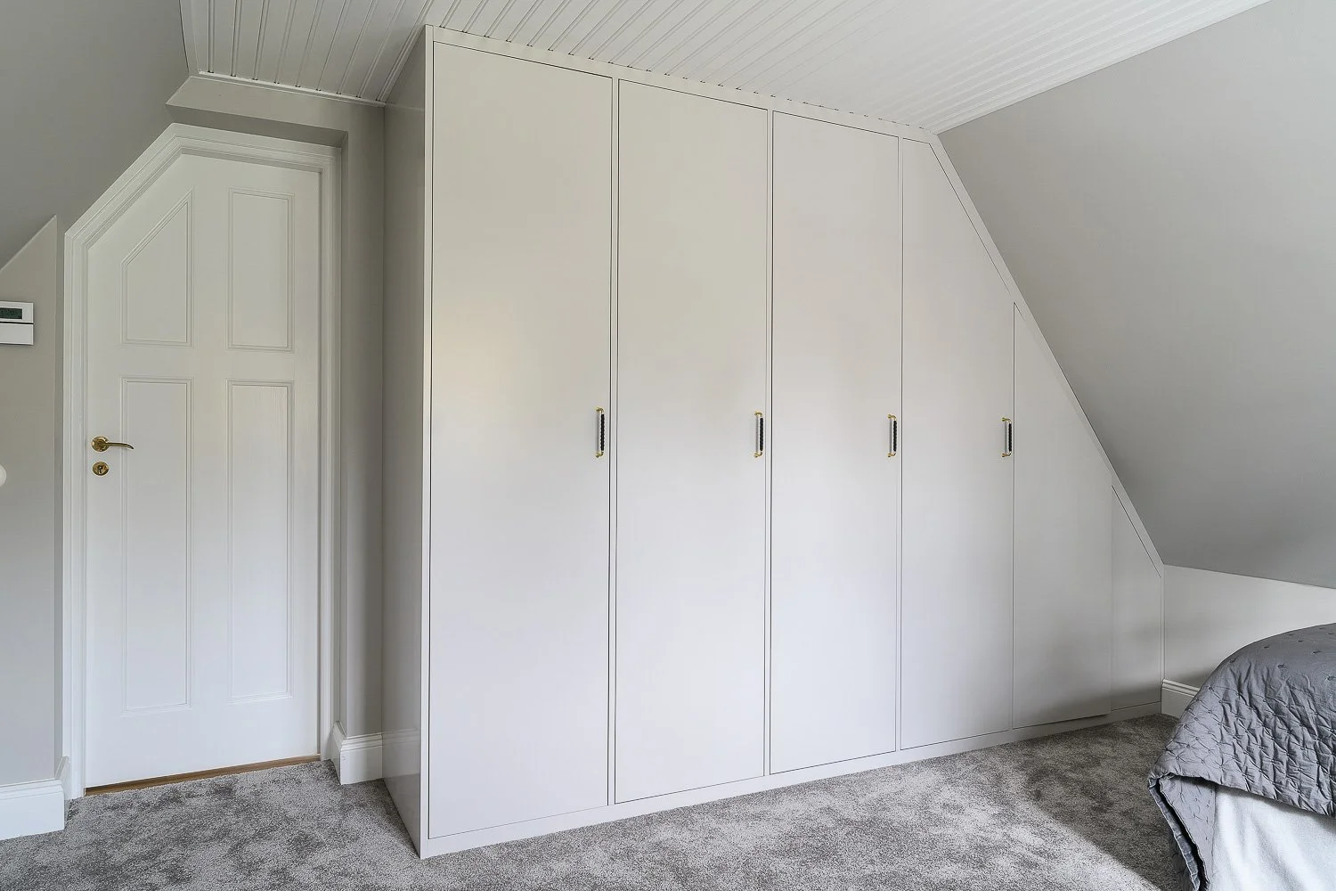 Platsbyggd garderob under snett tak – slanka luckor med laderhandtag i Djursholm.