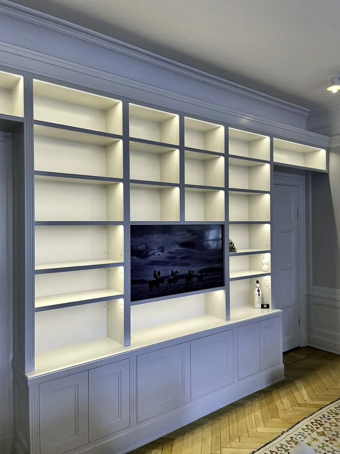Platsbyggd bokhylla med integrerad TV och stilren LED-belysning i vardagsrum i Stockholm