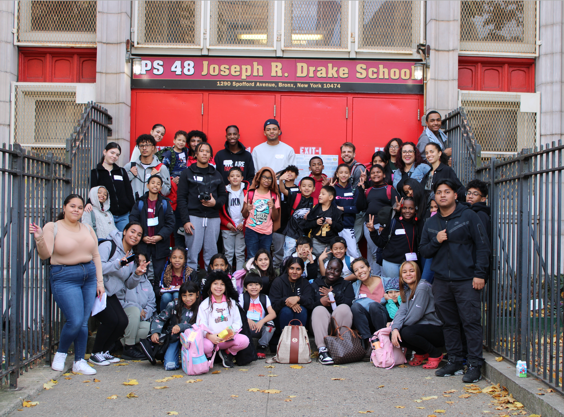 A large group of children and adults gathered outside a school building with a red door, posing for a photo.
