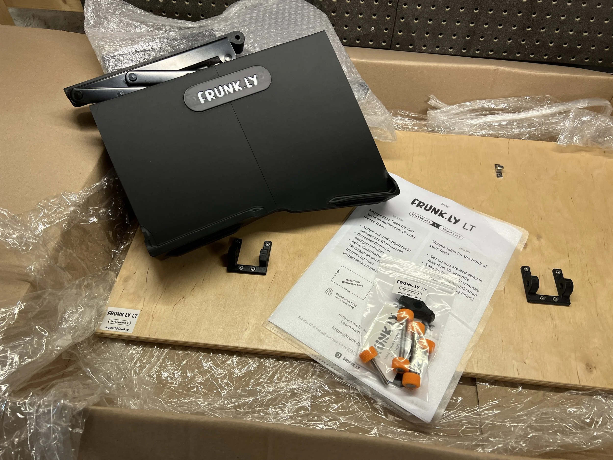 A set for the installation of a Tesla Frunk with instructions, mounting parts and a black carrying handle on a wooden table