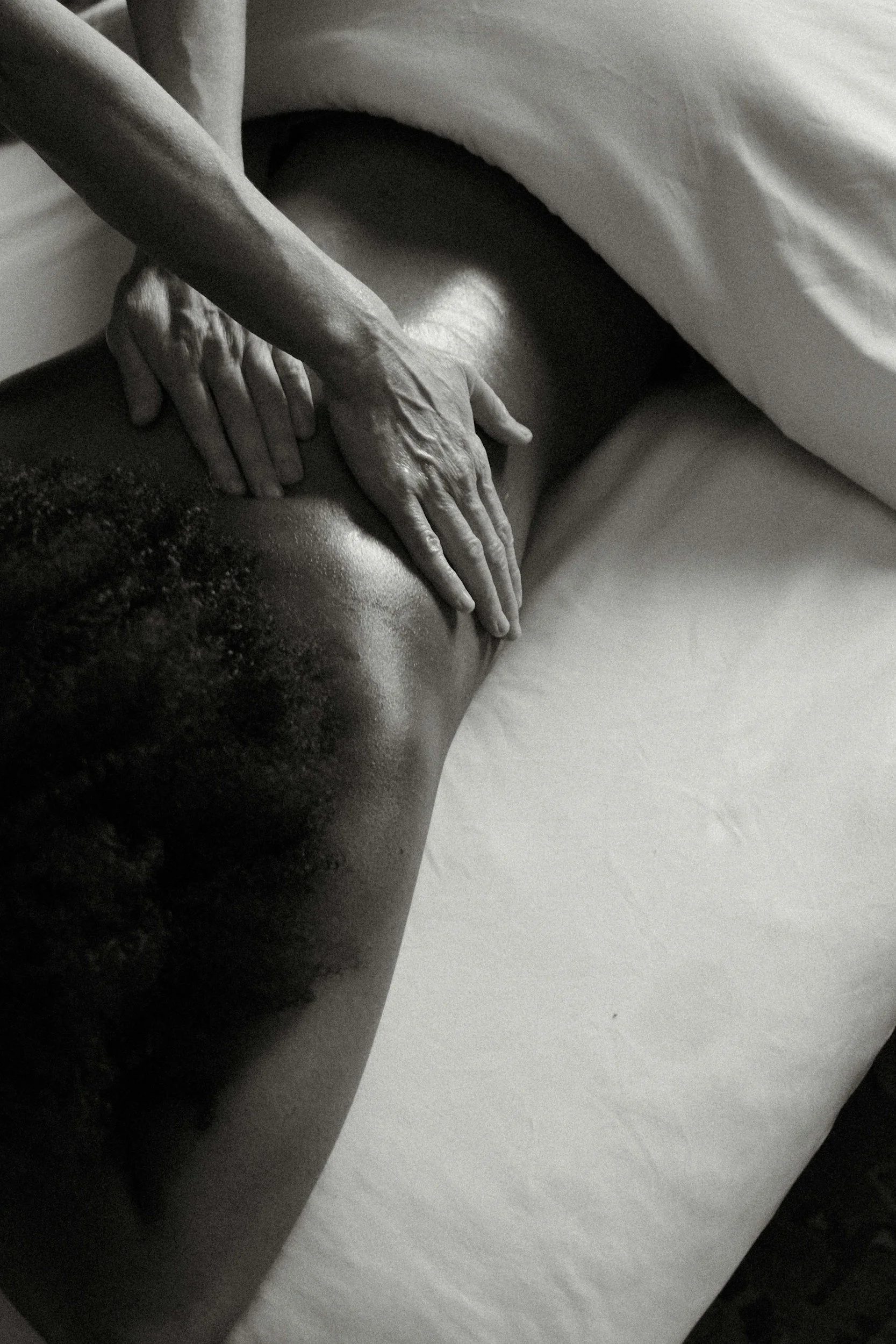 Close-up black and white photo of a person's hands gently resting on their abdomen, with a white sheet covering part of their body.