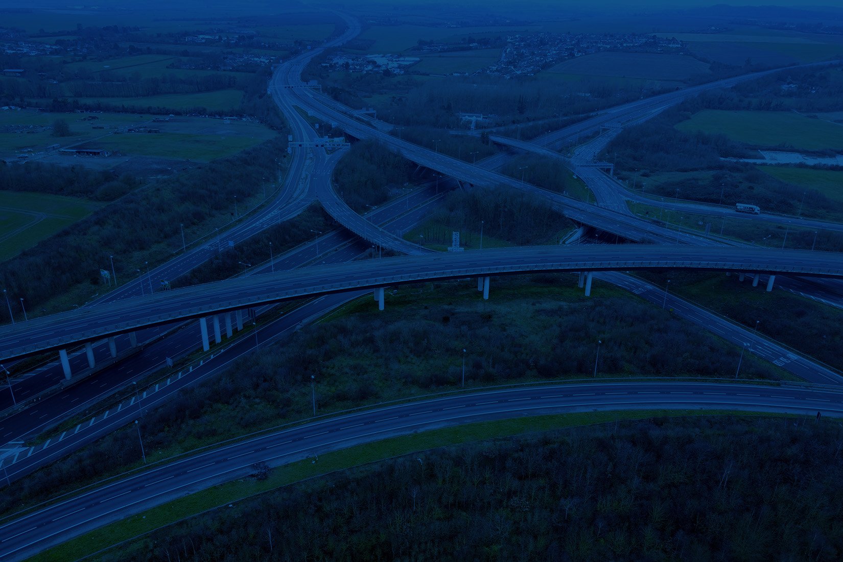 An aerial view of a complex highway interchange with multiple bridges and ramps over green landscape at dusk.