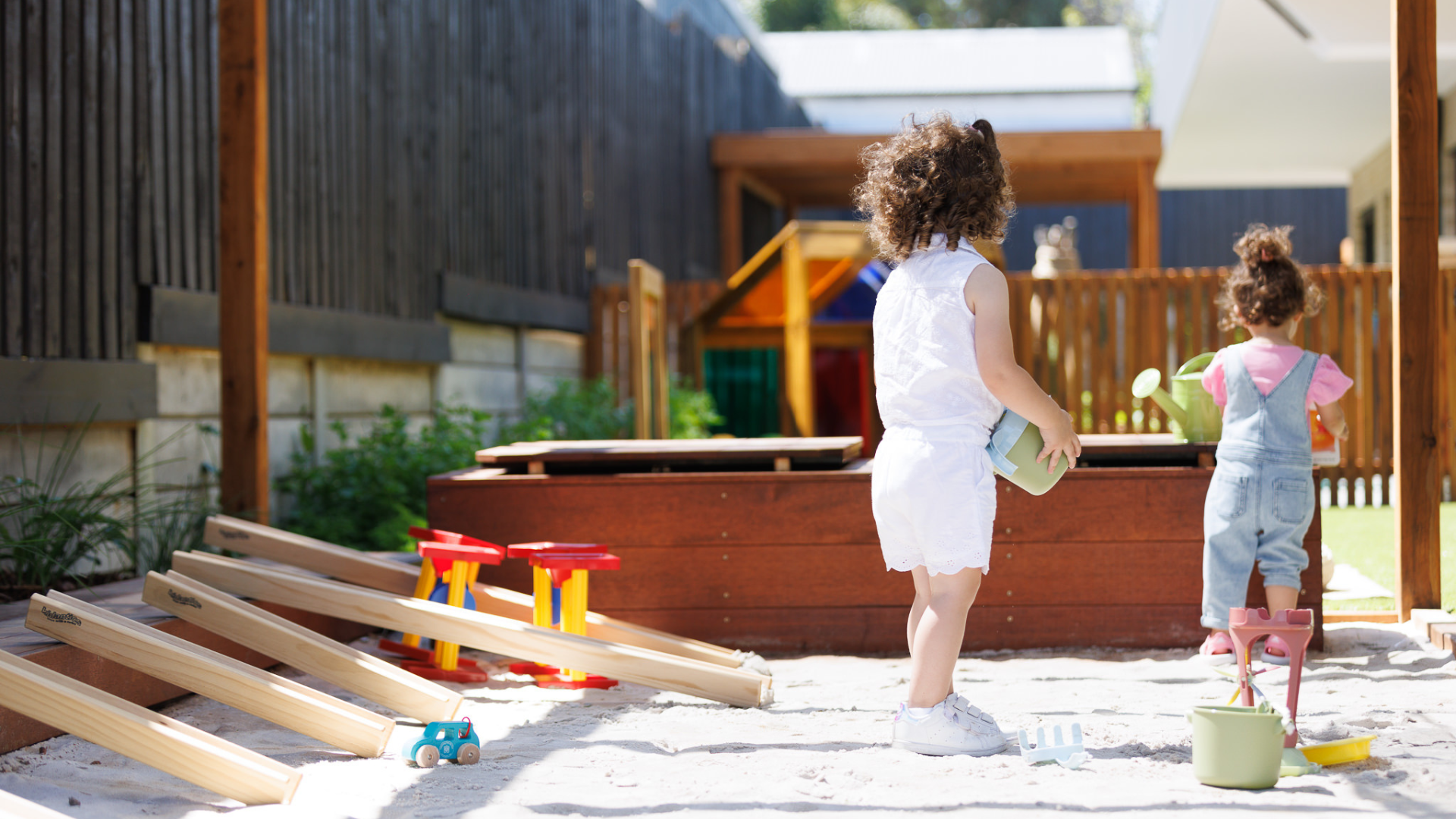 Modern two-story building with large windows, a front yard with trees, and people walking nearby under a clear blue sky.