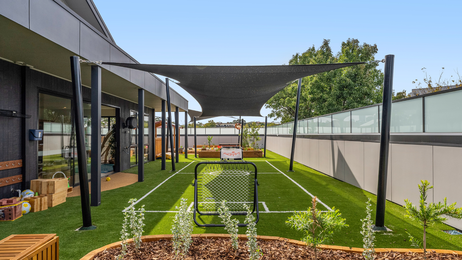 A long outdoor walkway lined with garden beds and greenery at Treetop Early Learning. This area provides opportunities for outdoor exploration, movement, and sensory experiences in a natural environment.