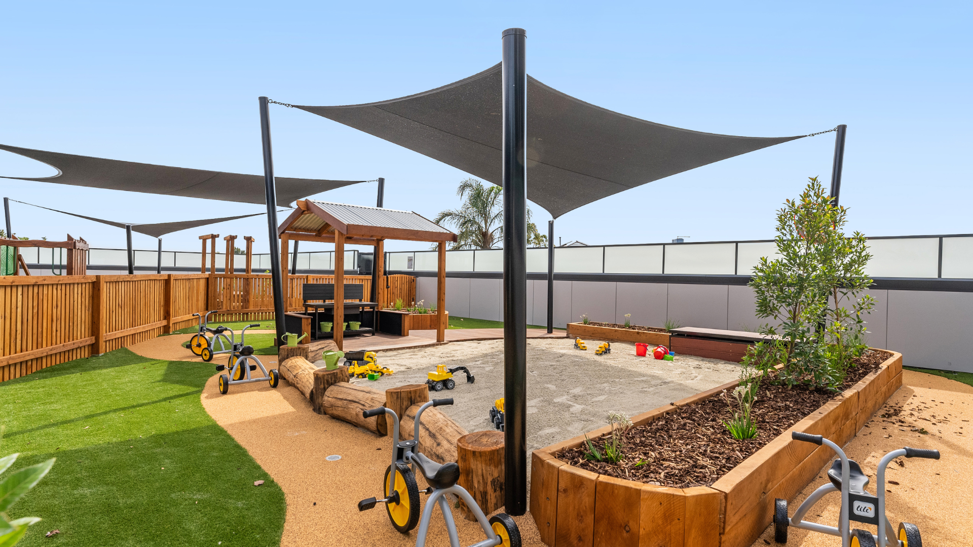 The outdoor play area at Treetop Early Learning features raised garden beds, timber play structures, and large shade sails. This space encourages active play, exploration, and connection with nature in a safe, sun-protected environment.
