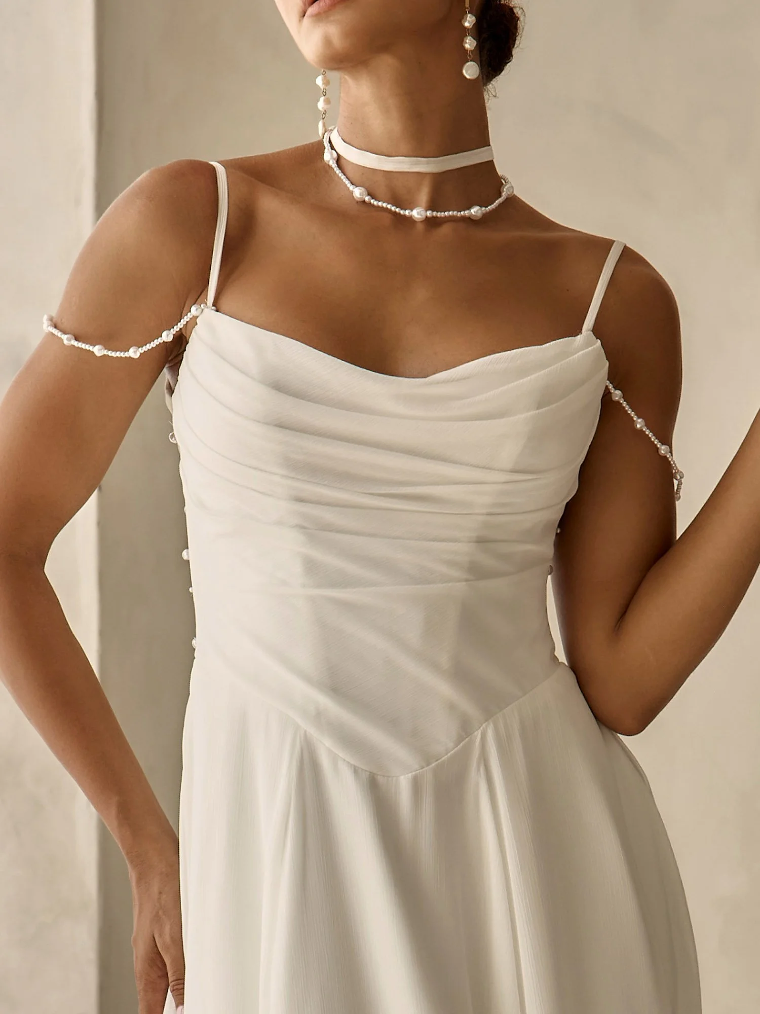 Minimalist chiffon A-line wedding dress with scoop neckline, pearl-beaded drape straps, pleated bodice, illusion back, Basque waist, leg split skirt, button train, and pearl collar accessory.