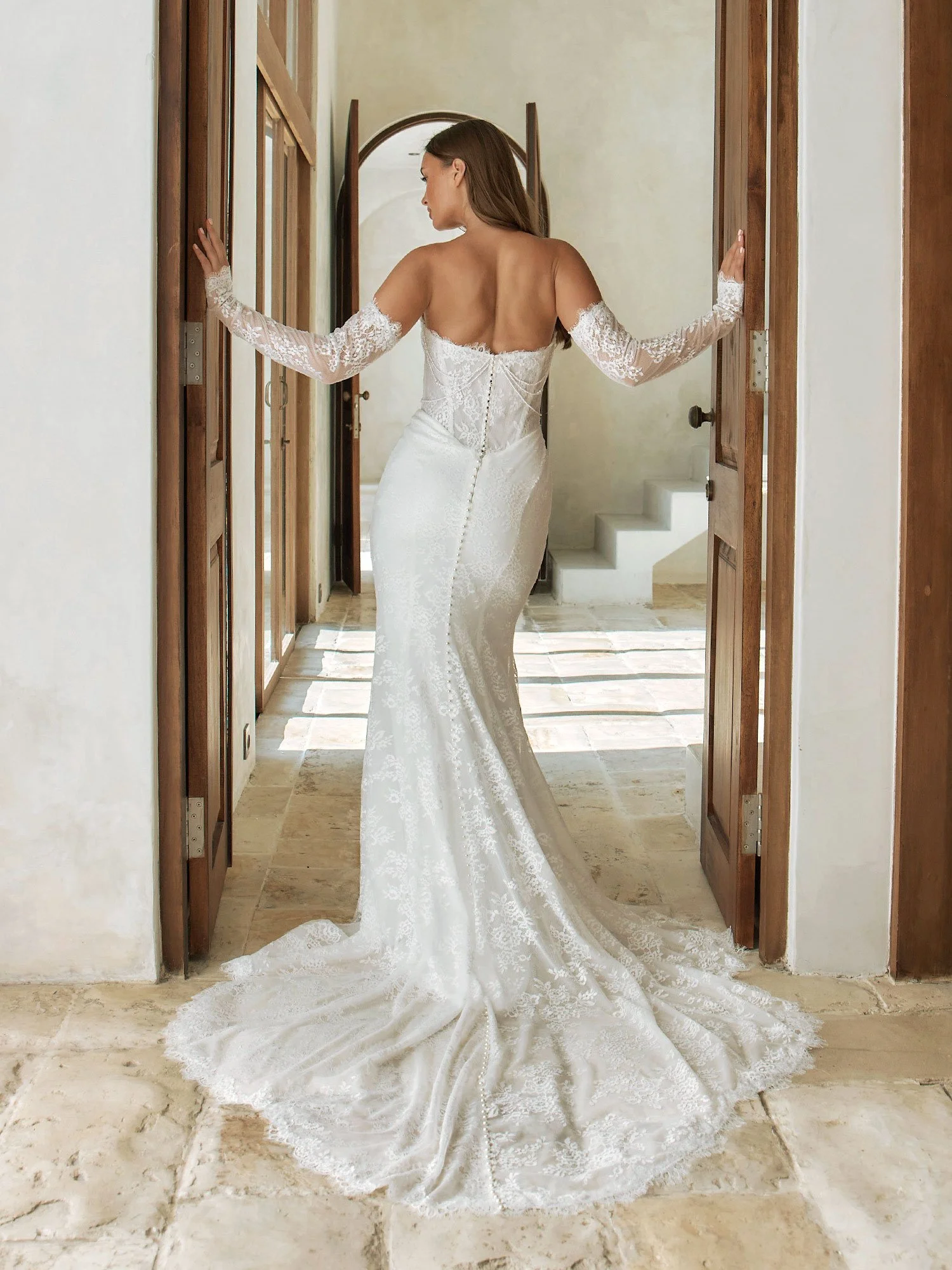 A strapless Chantilly lace wedding dress with a scoop neckline, draped pearl detail, exposed boning, Basque waist, fit-and-flare skirt, and a full illusion lace train