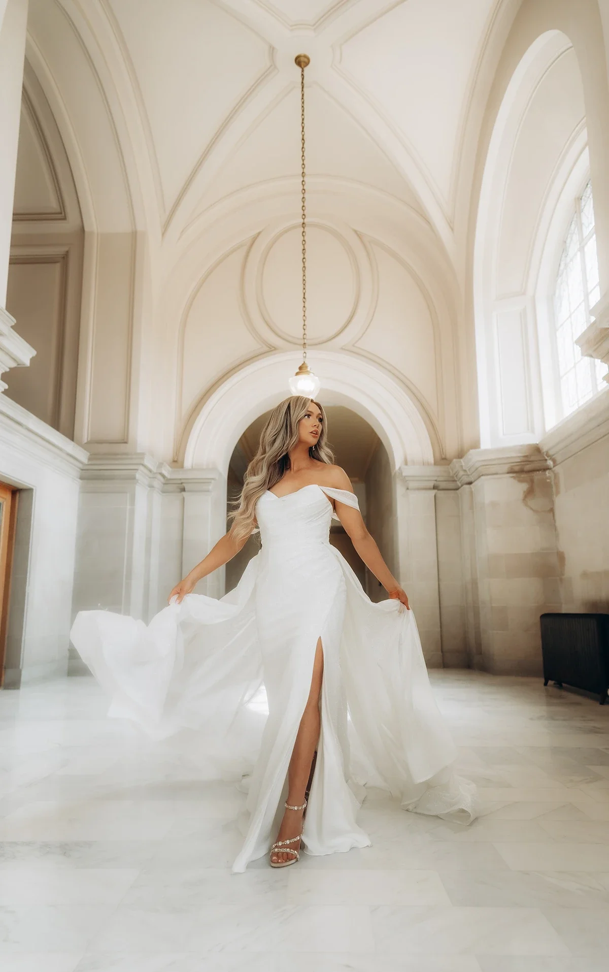 An allover glitter tulle fit-and-flare wedding dress with detachable off-the-shoulder straps and optional overskirt