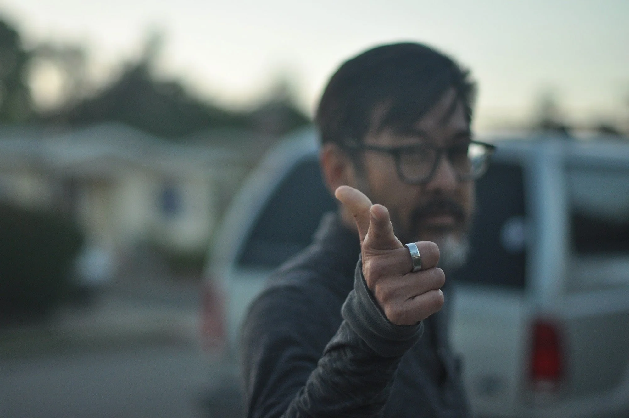 Chiropractor Koichi Naruishi, an Asian man with glasses and a beard, points his finger at the camera