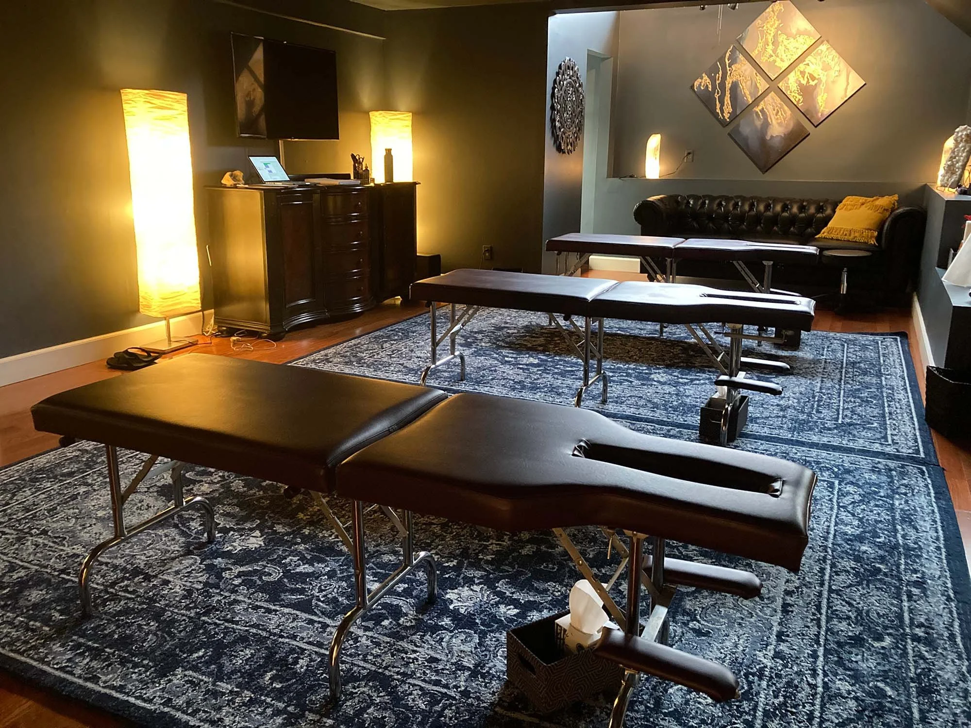 Three dark brown chiropractor tables sitting on a dark blue rug in a dimly lit office in Encinitas, California