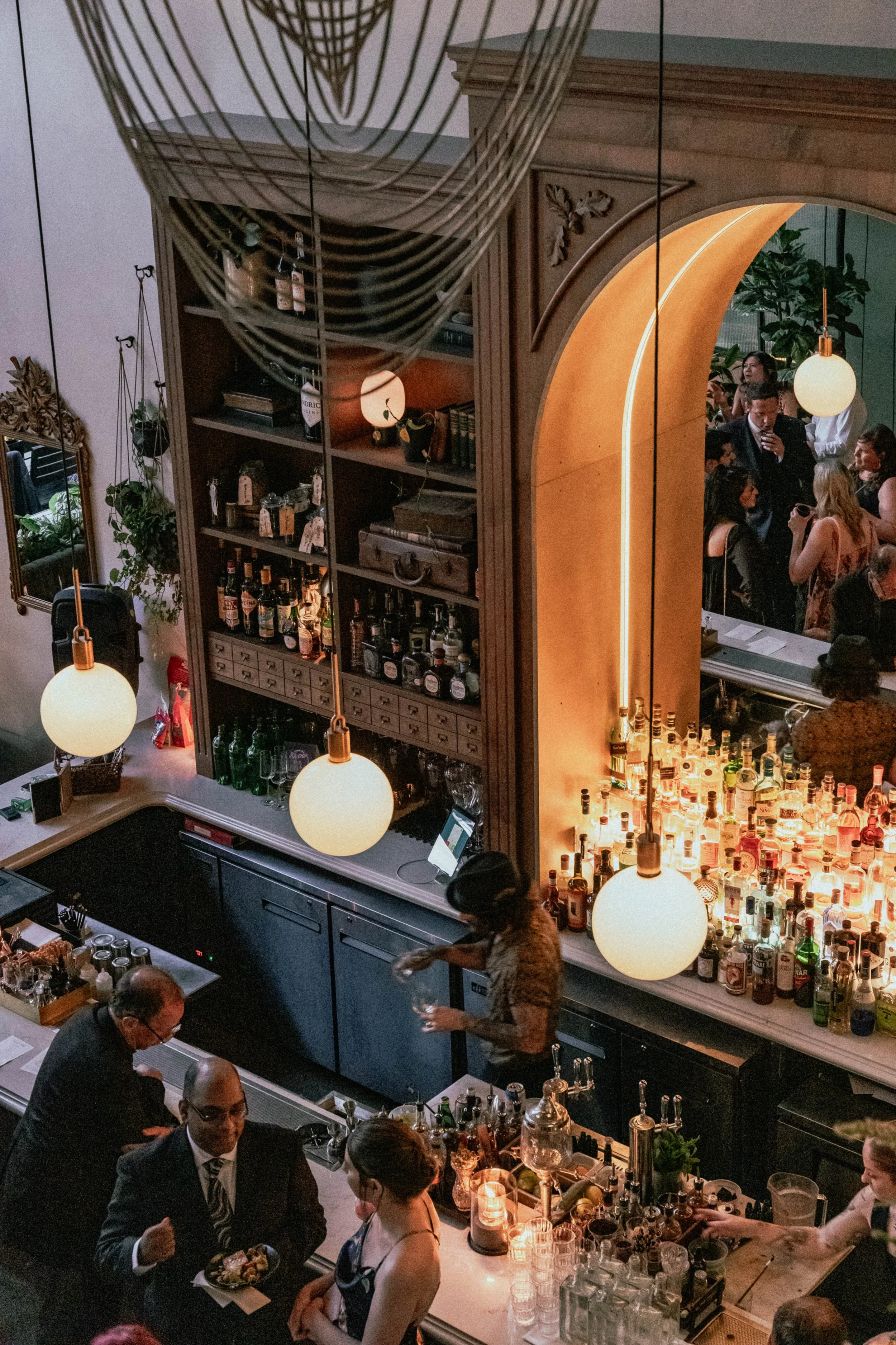 A busy bar scene with bartenders mixing drinks, a crowd of people socializing, and a well-stocked bar illuminated with warm lighting.