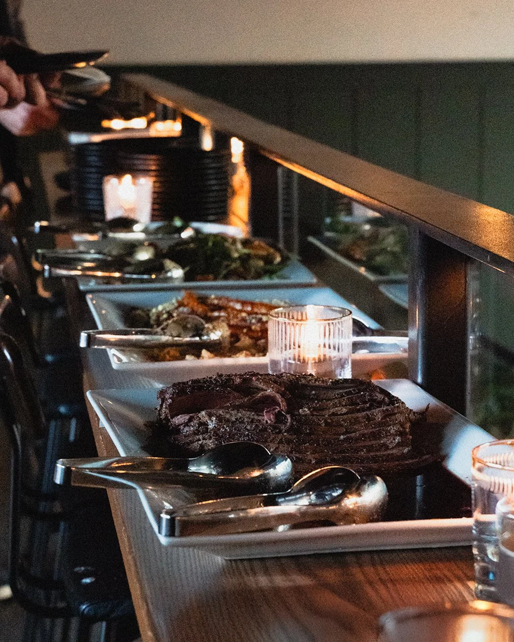Buffet table with slices of cooked steak, various seafood dishes, and side dishes, set in a dimly lit setting with small candles, part of a wedding held at The Watson