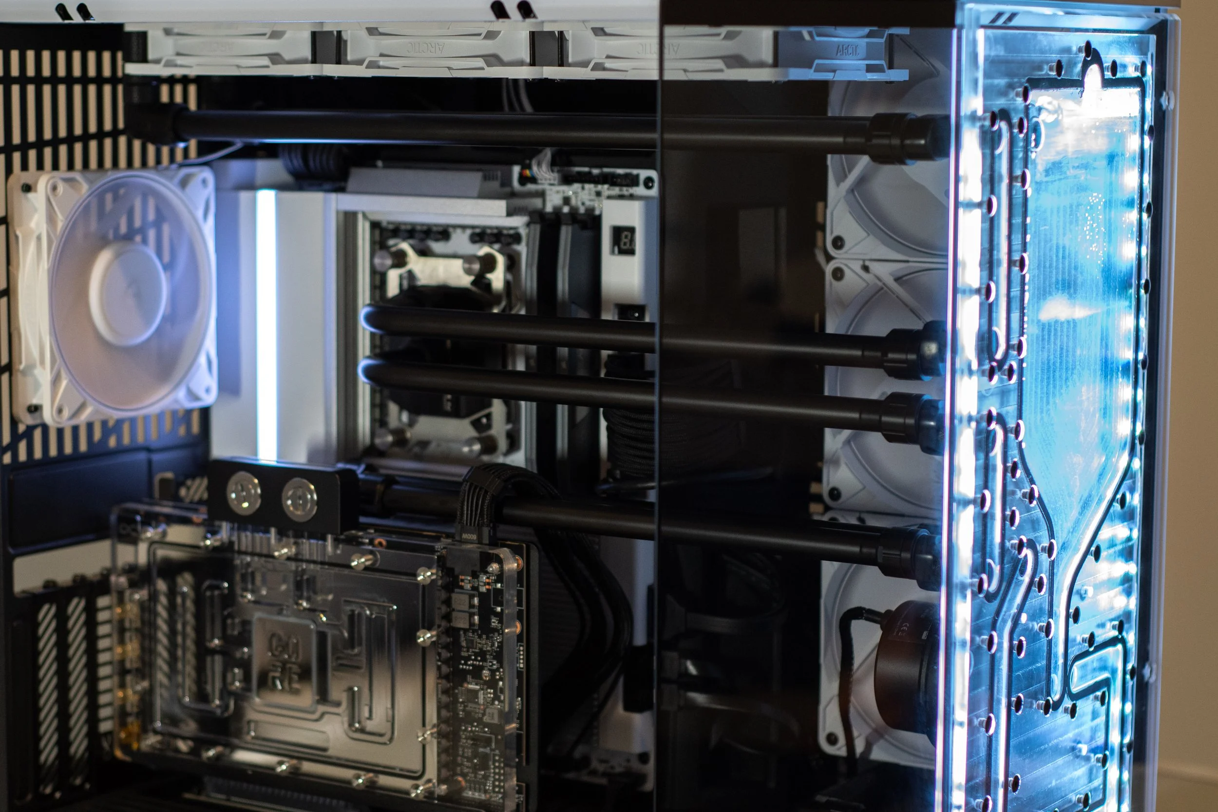 A custom-built gaming computer with a water cooling system, featuring black tubes, radiator, white fans, and illuminated blue LED lights.