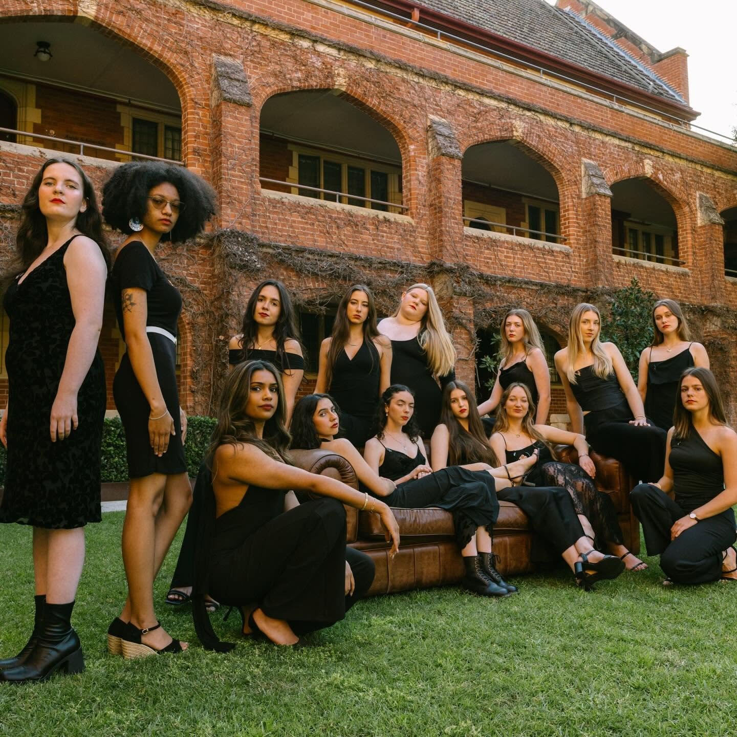 14 young women sit on a brown leather couch in the quadrangle of St George's College.