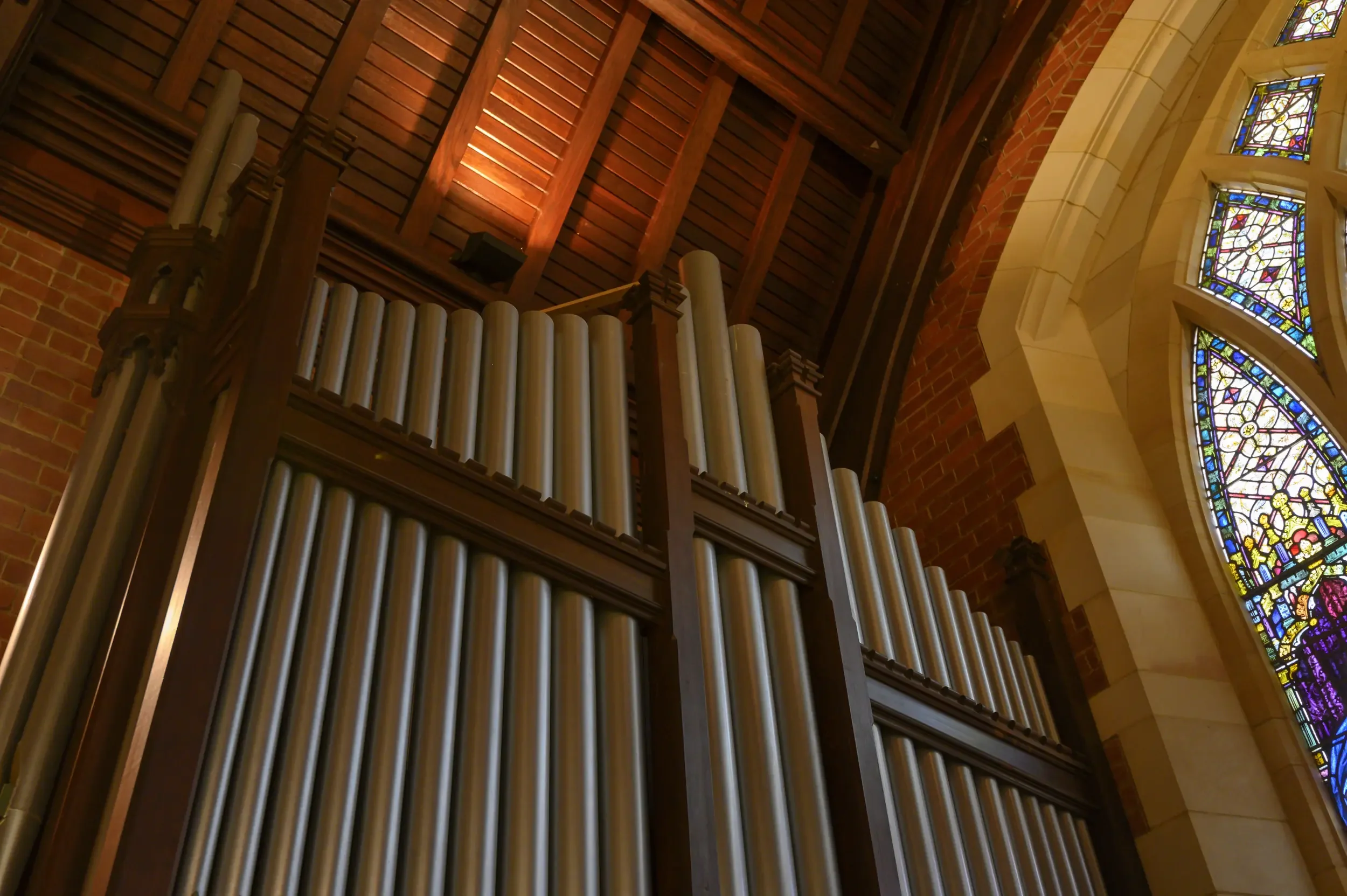 The pipes of the organ at St George's College with a stained glass window to the right.