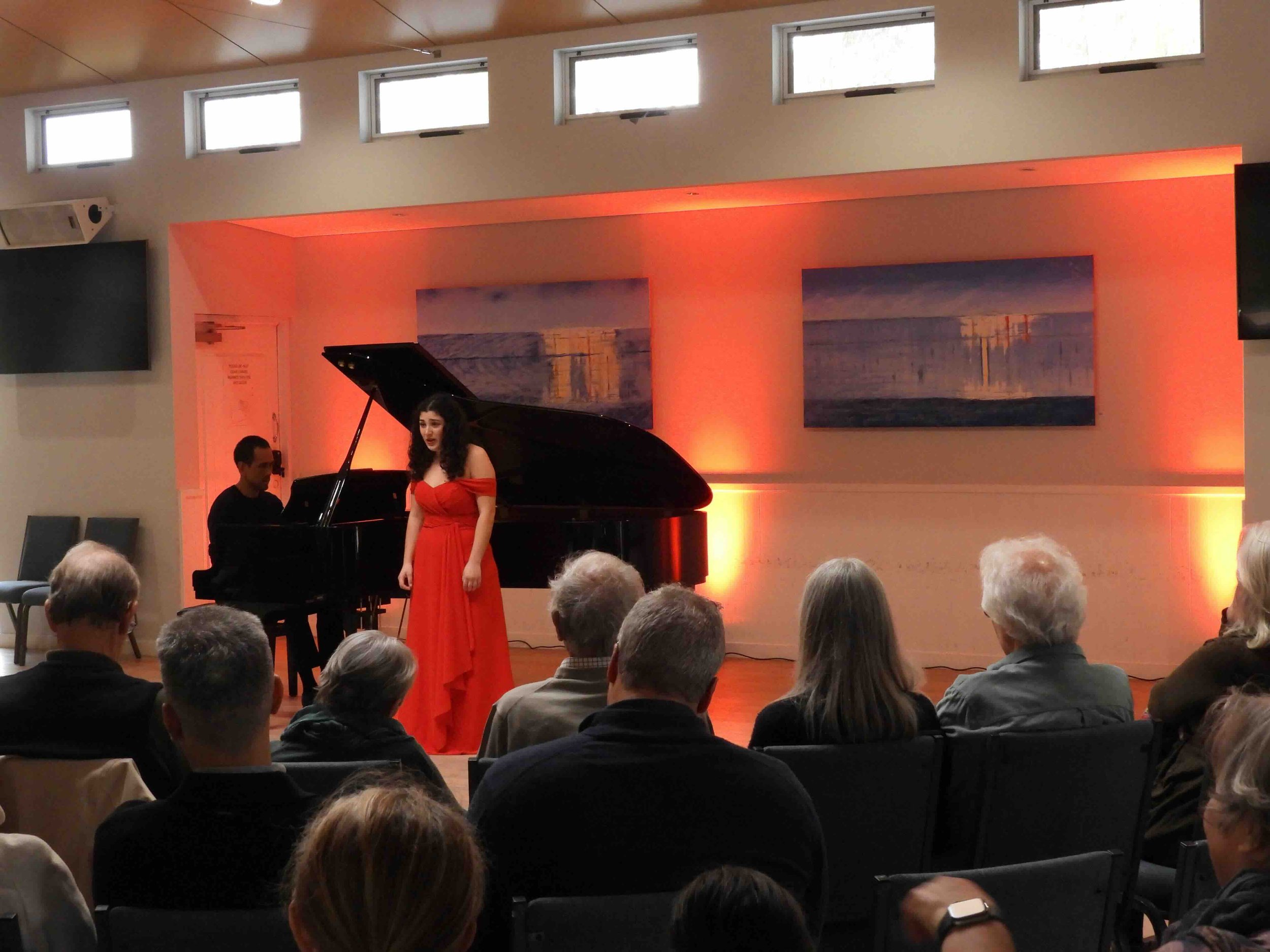 Raymond Yong and Tiani Glasgow perform in front of a red lit wall.