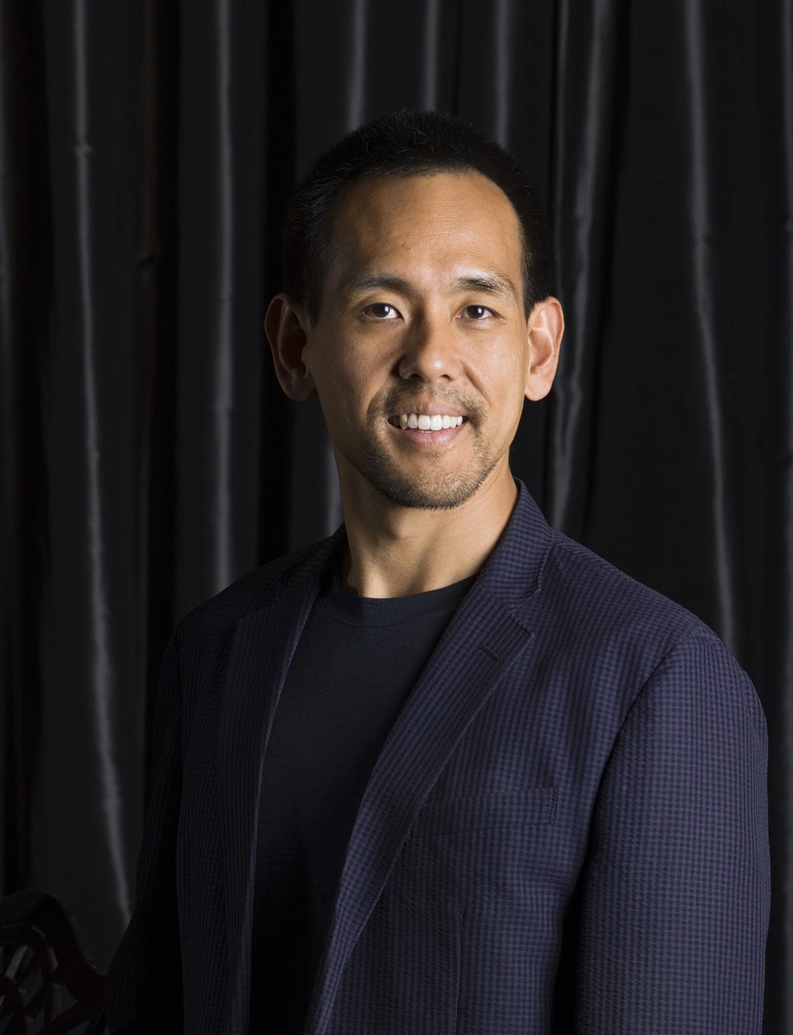 Raymond Yong standing in front of a black satin curtain.