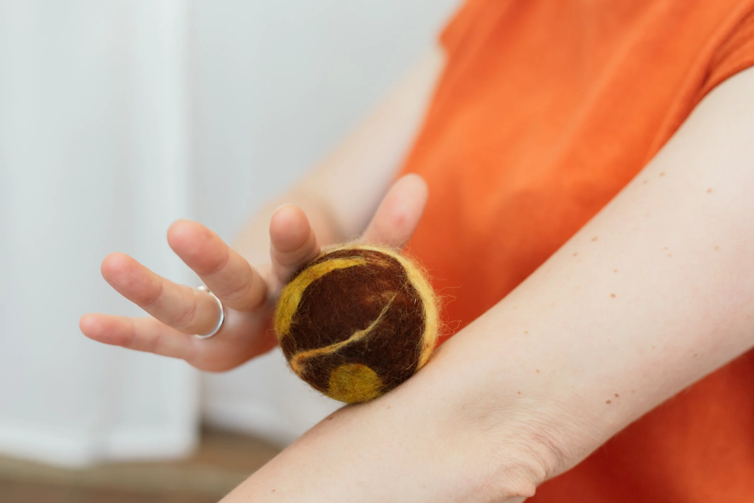 Vrouw met oranje kleedje is de ademtrainer van Adem Je Fit die tijdens een sessie in Antwerpen laat zien hoe je met de huid werkt door een zachte gekleurde vilten bal over je arm te rollen.