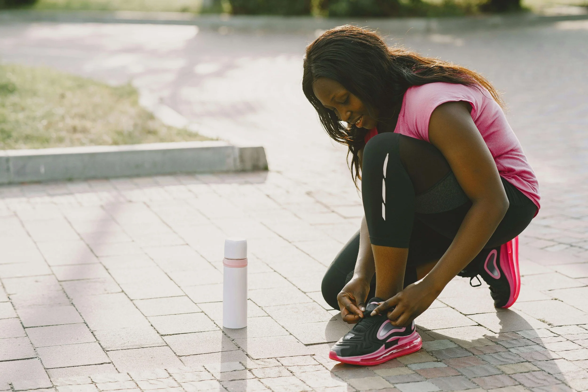 Amara is klaar om te gaan joggen, ze lacht en de zon schijnt. Ze start op de stoep en draagt een roze jogging outfit.