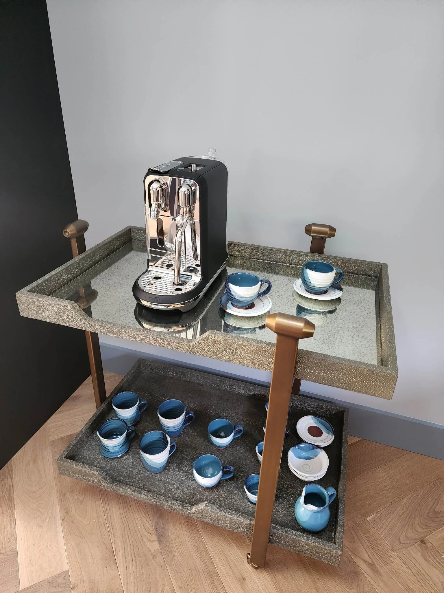 A coffee machine on a glass and metal cart with blue and white cups and saucers.