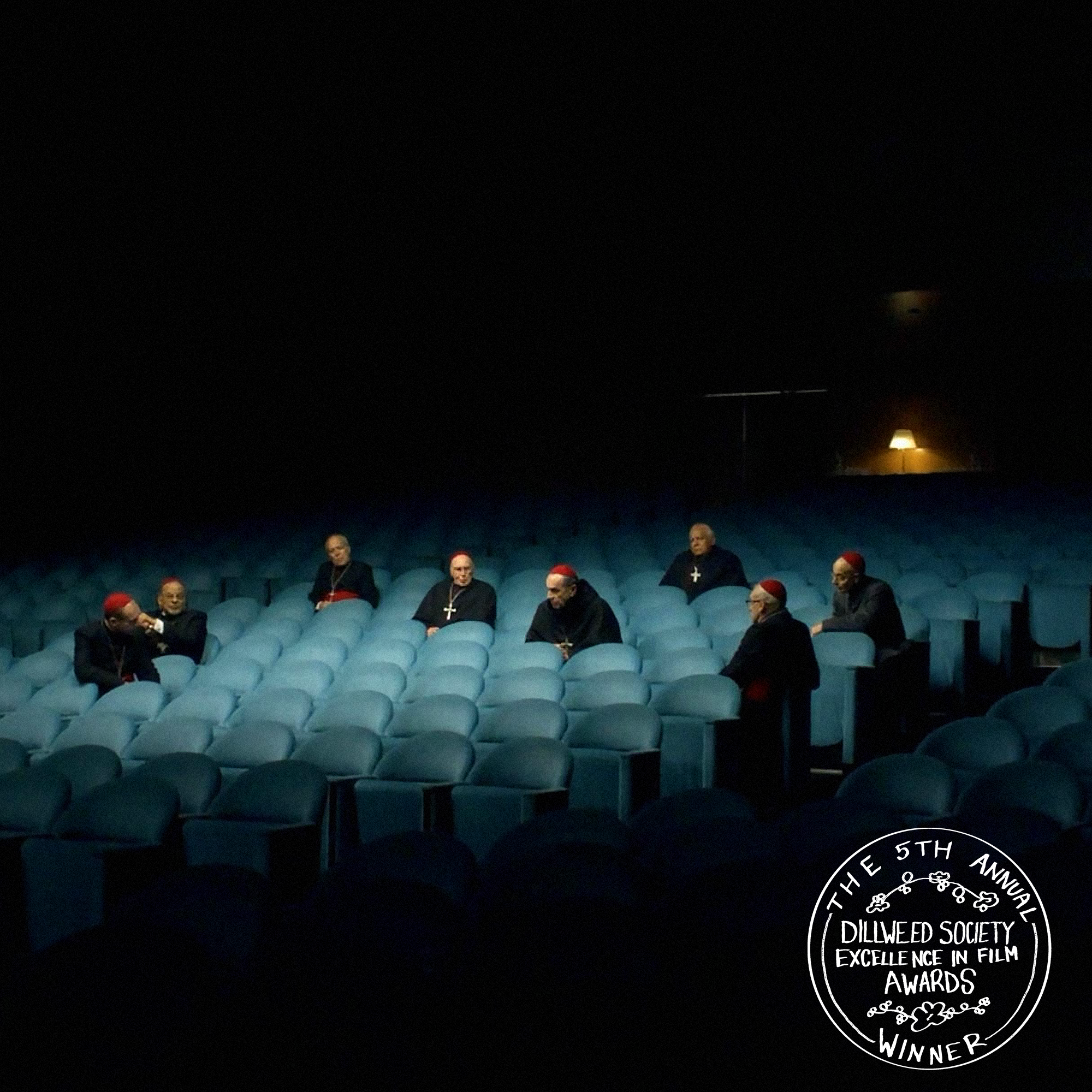 An empty movie theater with blue seats and eight men dressed as cardinals sitting separately throughout the theater, with a badge in the bottom right corner reading "The 5th Annual Dillweed Society Excellence in Film Awards Winner."
